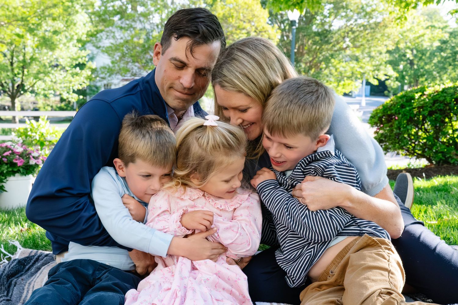 Loving family of five sharing a warm group hug on a blanket in a beautiful garden setting.