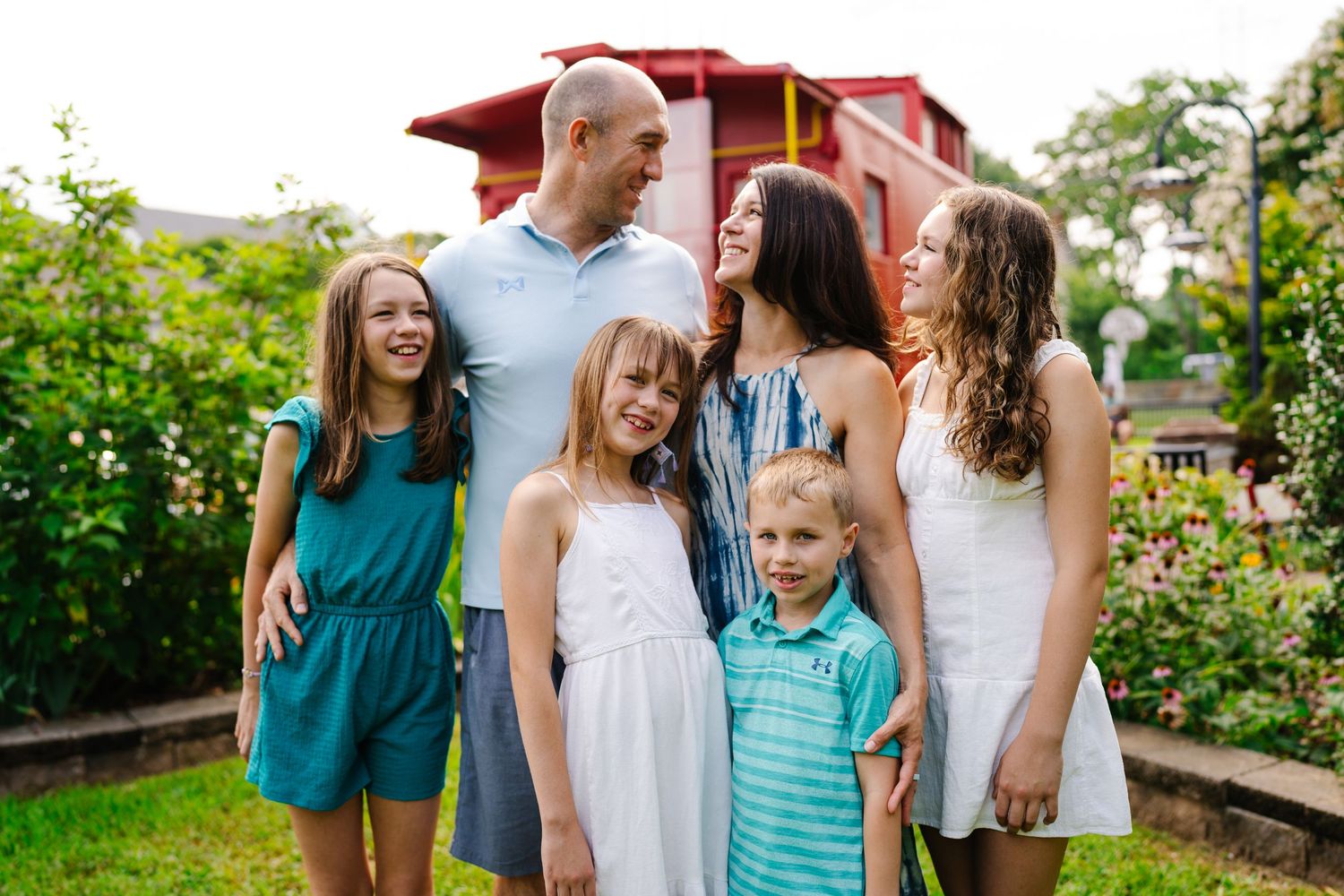 Happy family of six posing outdoors in a lush garden, wearing coordinated outfits in teal and white.