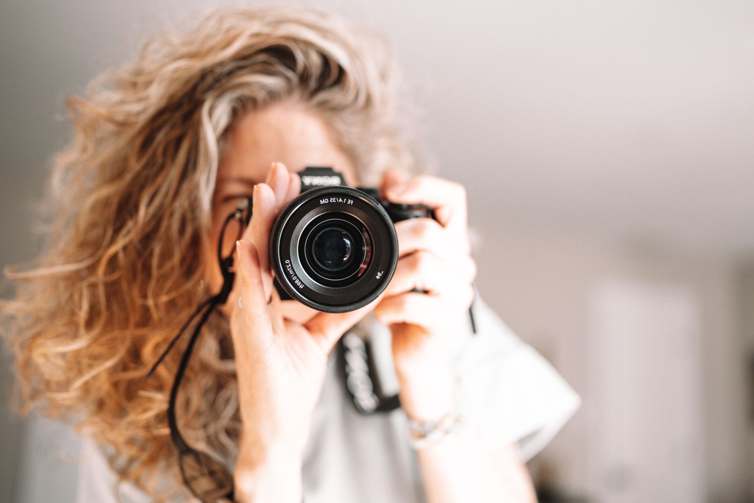 Woman photographer holding a DSLR camera up to her face outdoors.