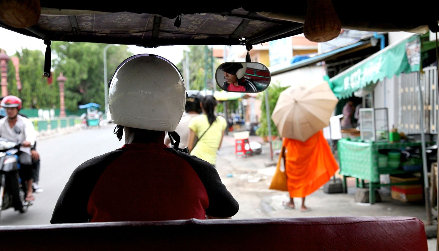 View from a tuk-tuk of a Buddhist monk in orange robes walking along a street in Southeast Asia.