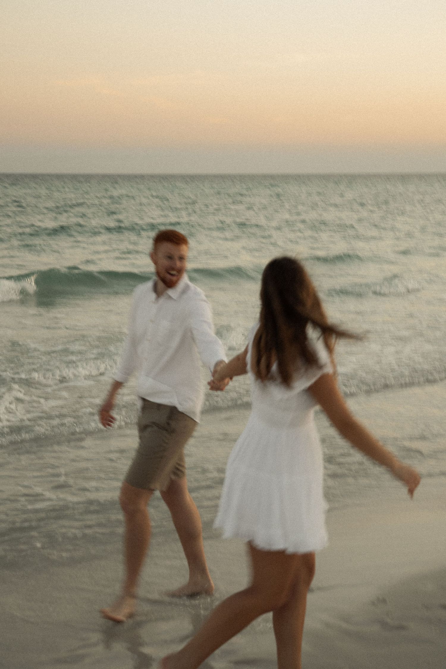 Couple playing and dancing together on beach during golden hour.