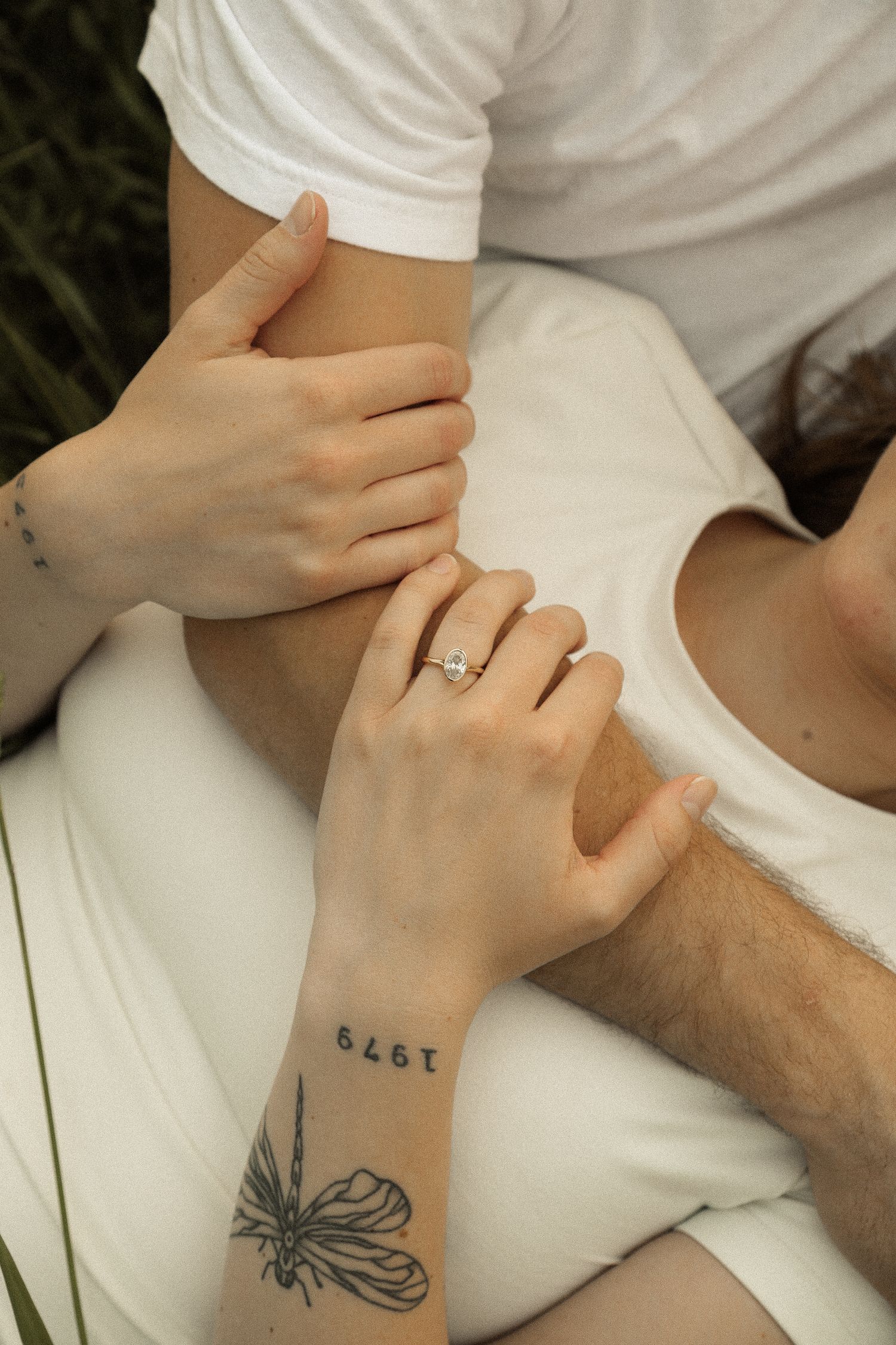 Close-up of intertwined hands with a butterfly tattoo and engagement ring visible.