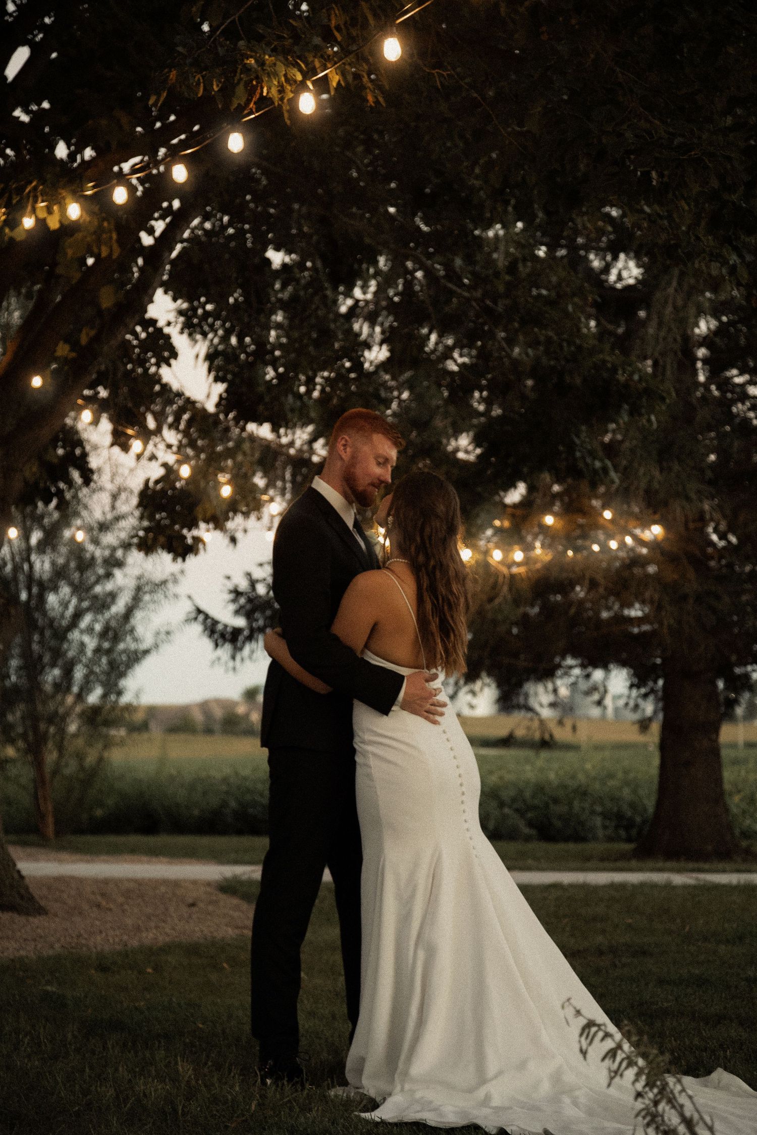 A romantic wedding photoshoot under trees with string lights at dusk.