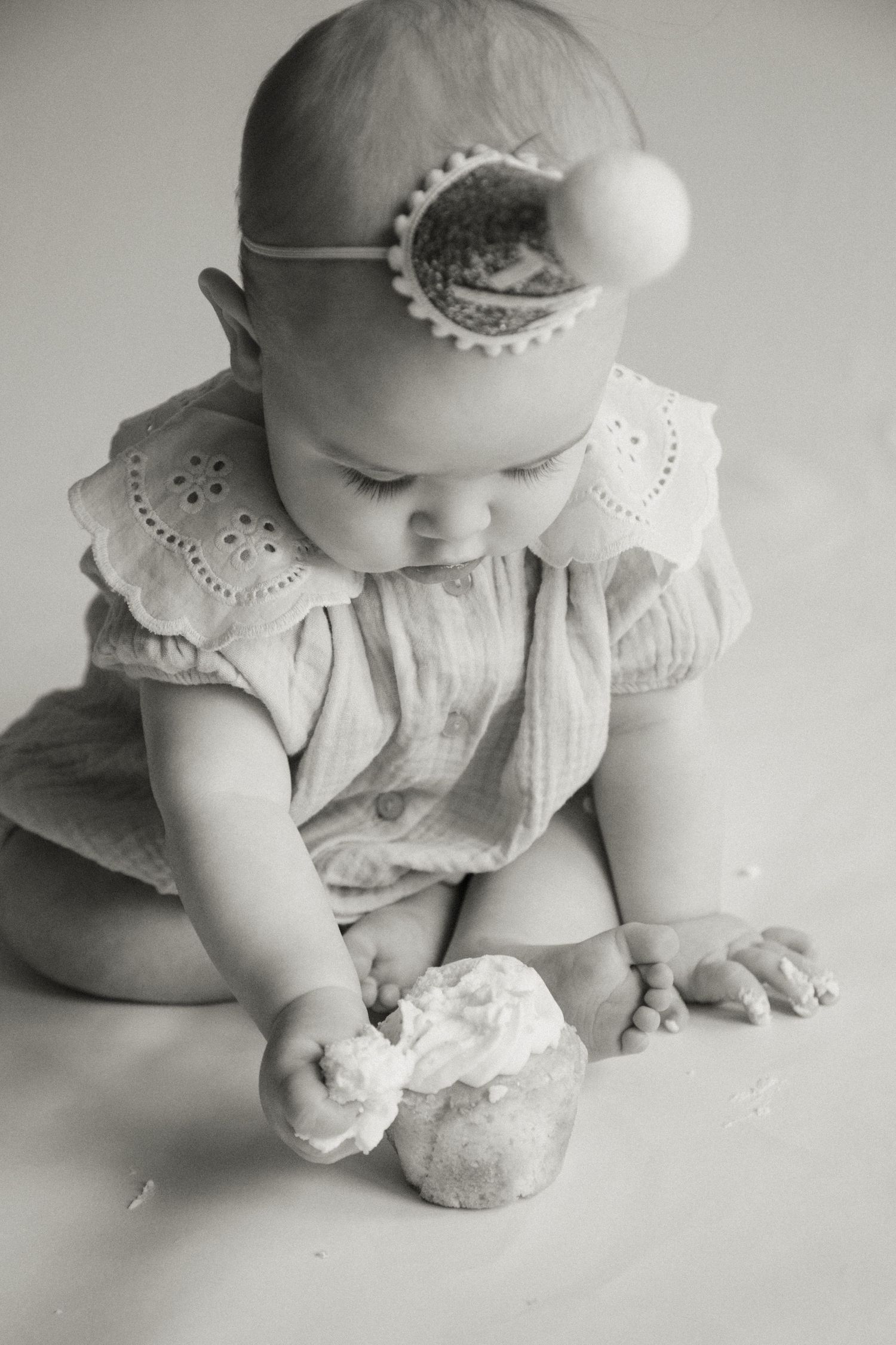 Adorable baby girl in headband exploring her smash cake in a classic black and white photo.
