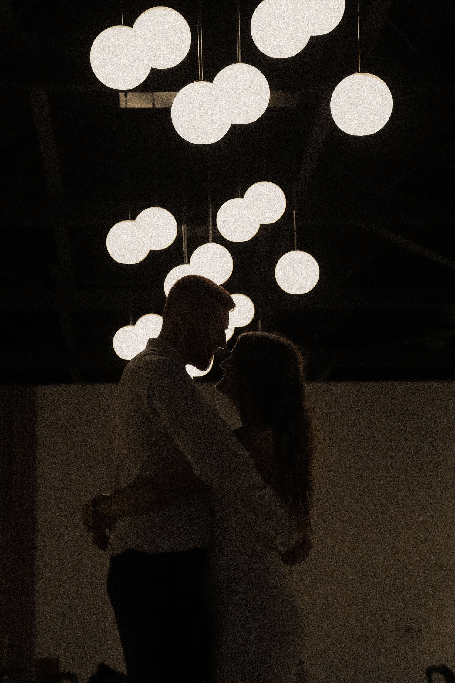 Silhouetted figures dance under glowing round paper lanterns in a dark room.