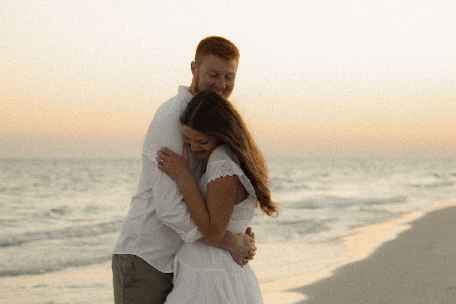A couple shares an intimate embrace on a beach during golden hour with waves in the background.