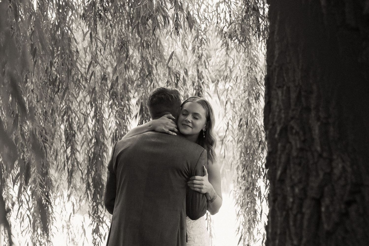 A tender embrace between newlyweds beneath drooping willow branches.