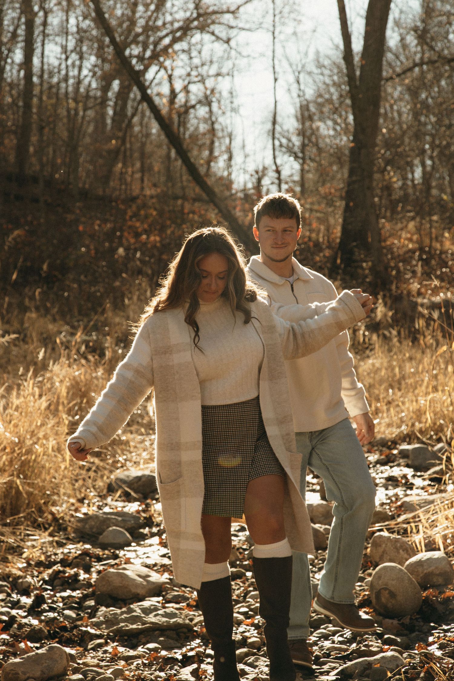 A couple walks together through an autumn forest trail with golden sunlight filtering through trees.