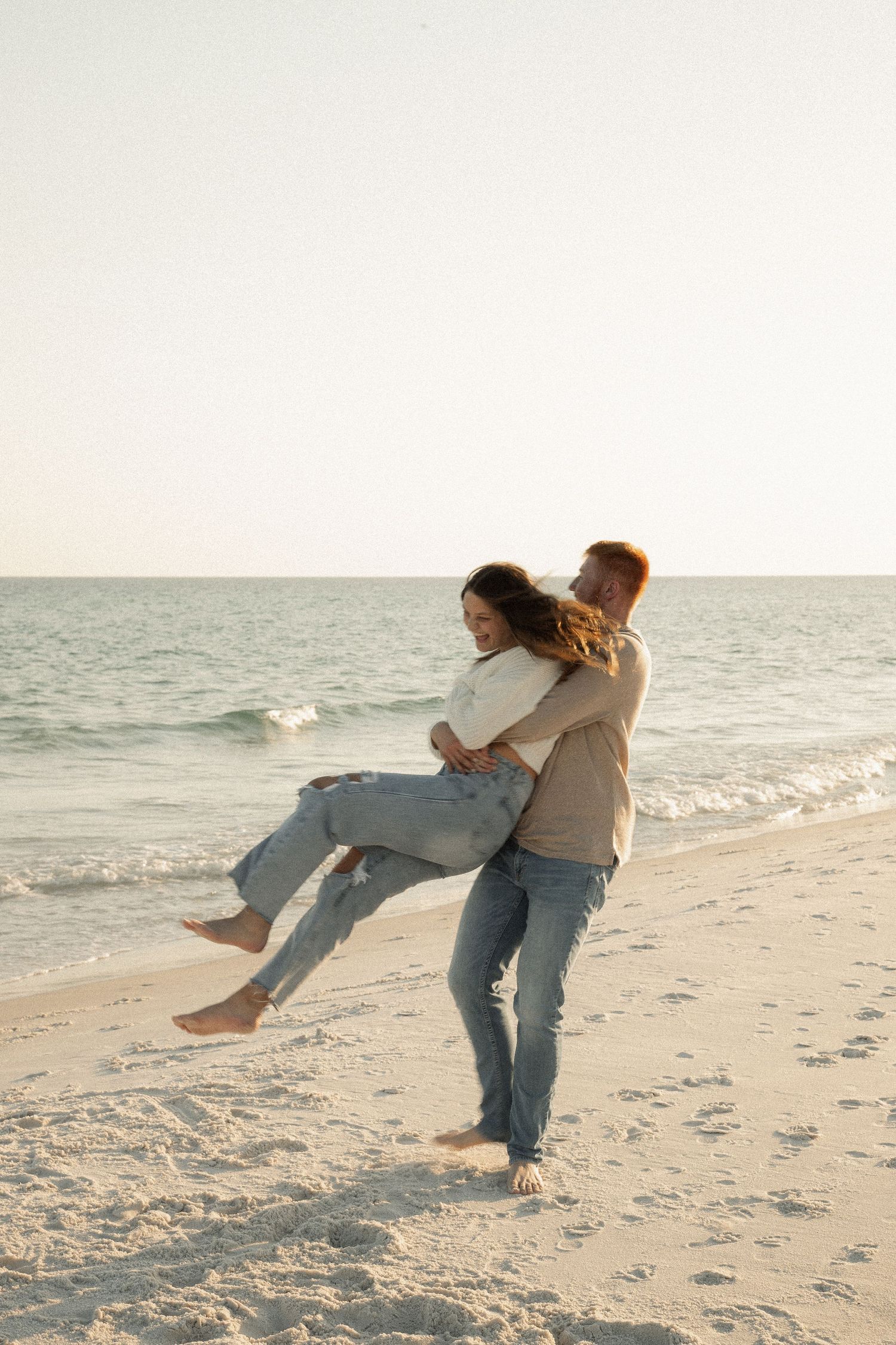 Couple playing and spinning on white sandy beach at sunset.