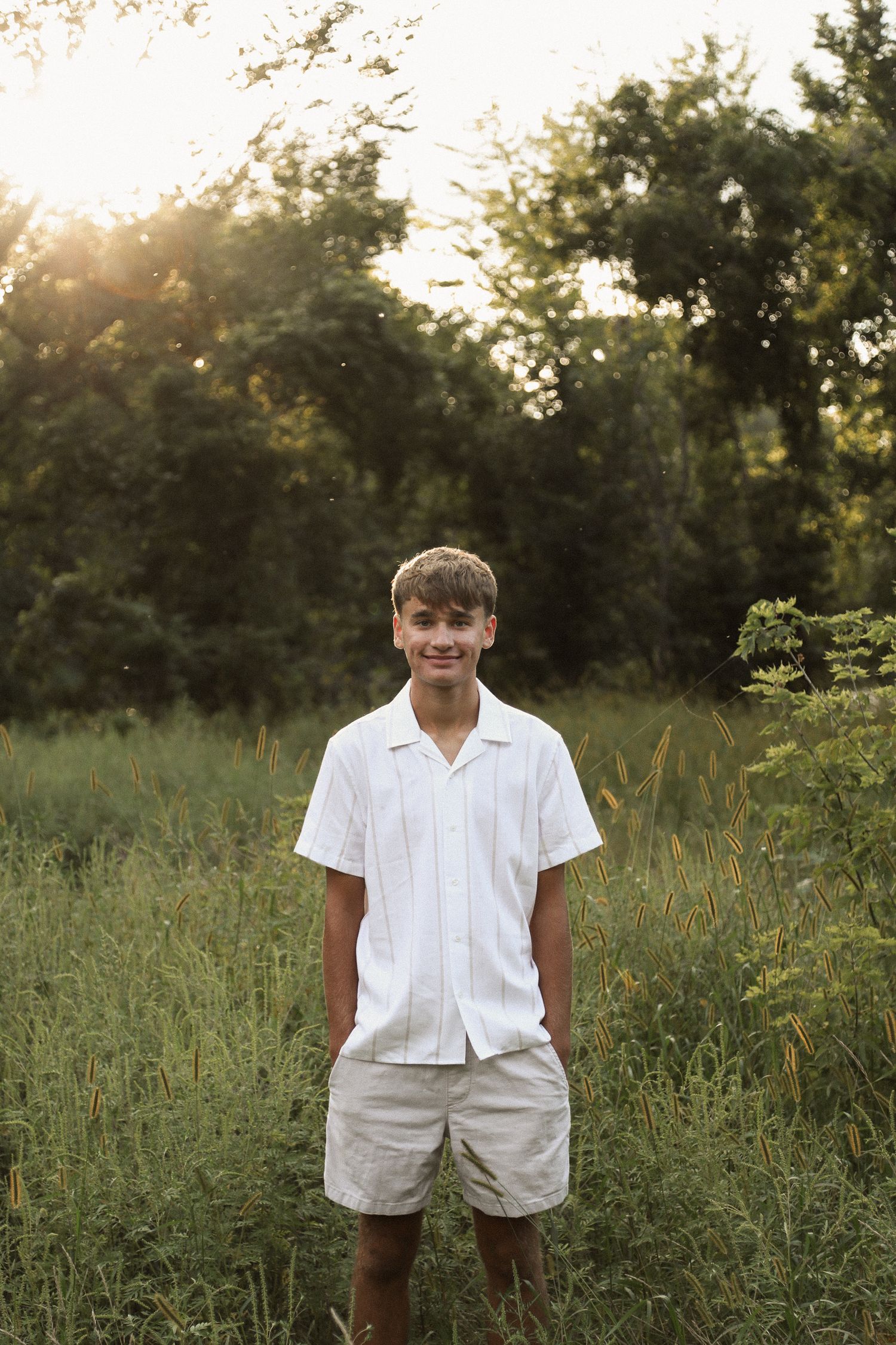Figure in all-white summer outfit stands in tall grass during sunset.