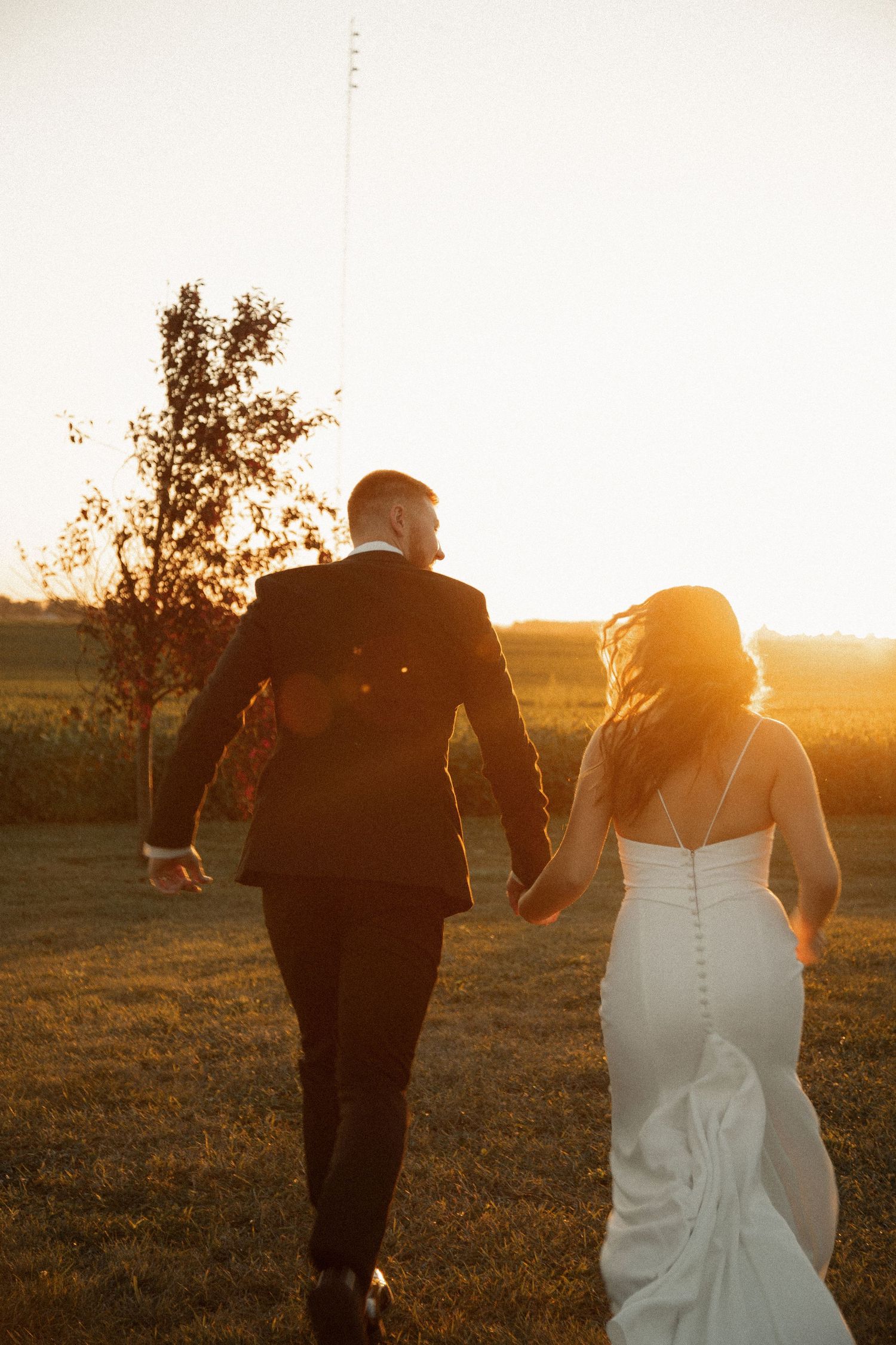 Couple walking hand in hand through a sunlit field at golden hour.