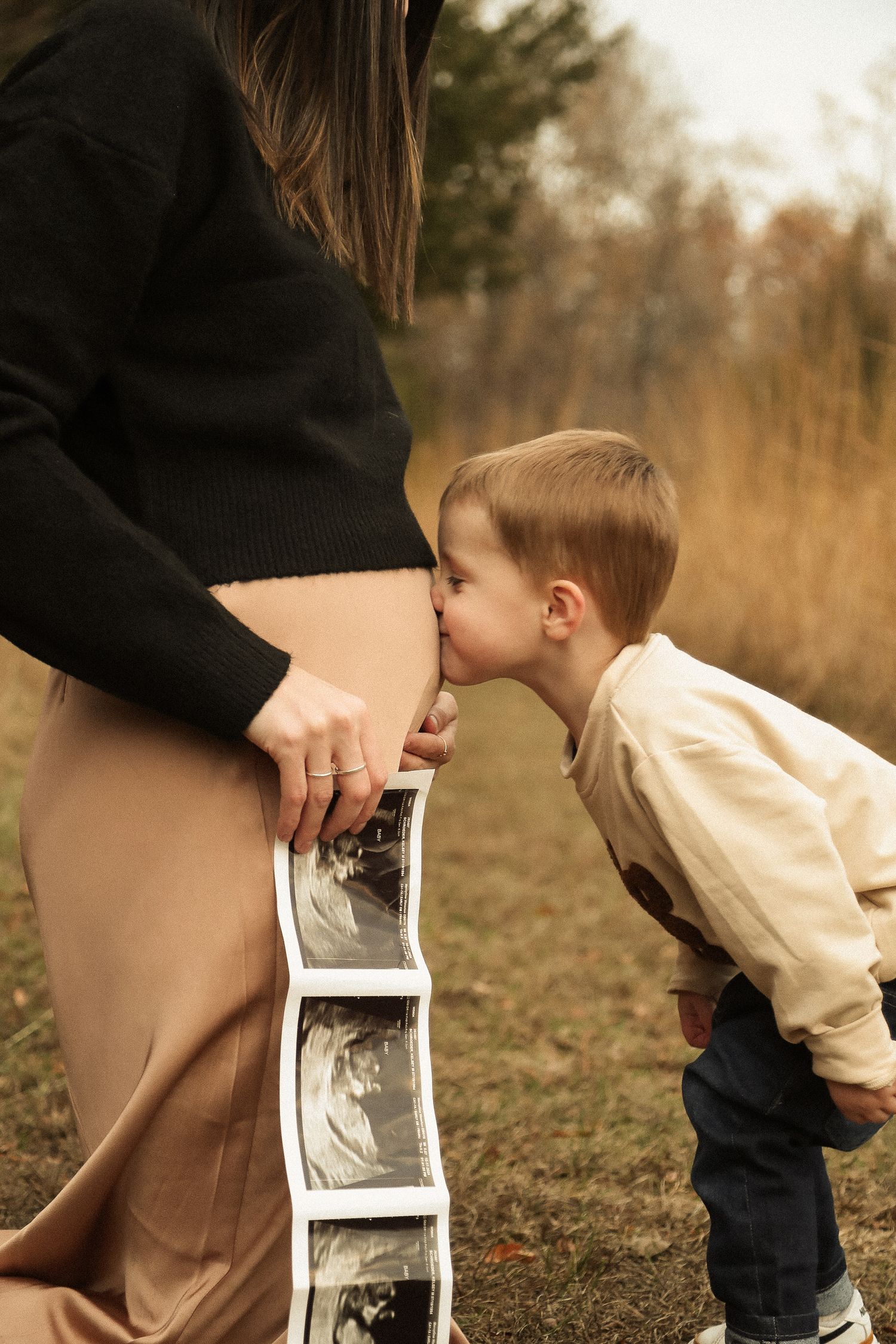 A young child kisses an ultrasound strip while standing next to someone in an outdoor setting.