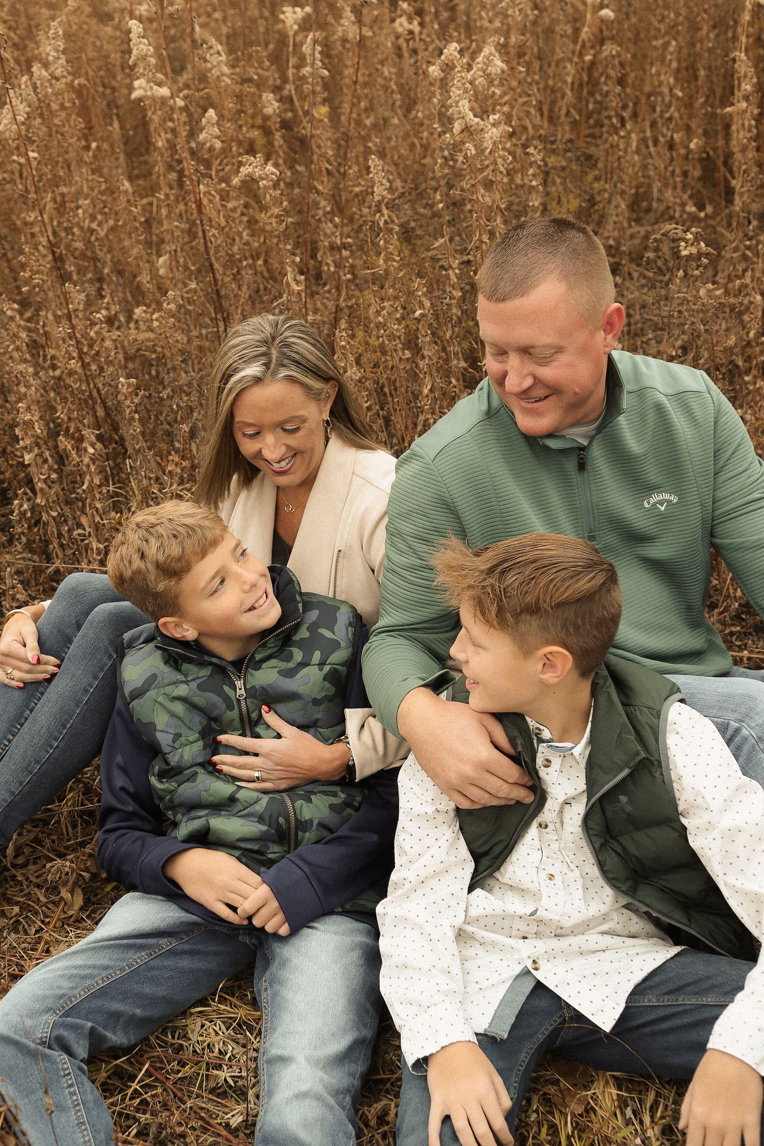 Family laughing and playing together while sitting in tall autumn grass.