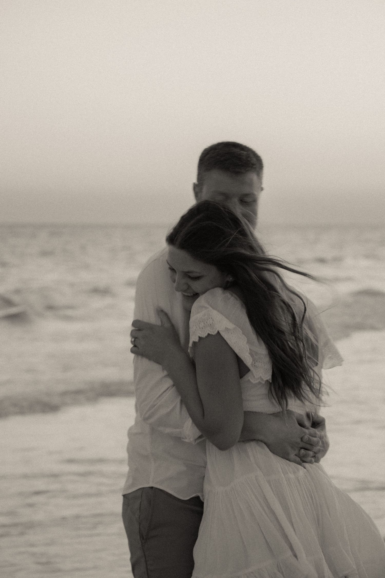 A tender black and white moment captured of a couple embracing on a misty beach.