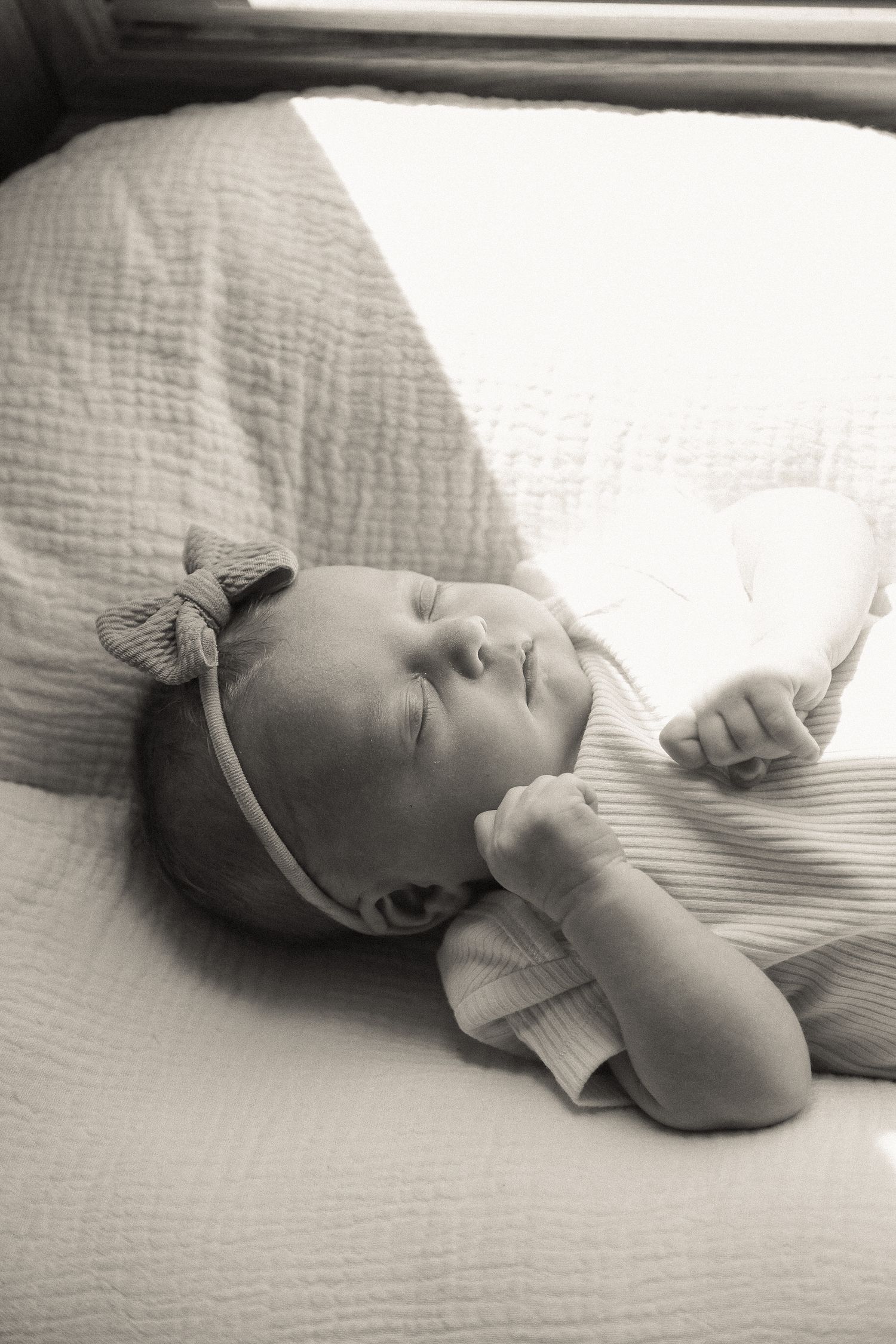 A sleeping baby in light clothing rests peacefully on white textured bedding.