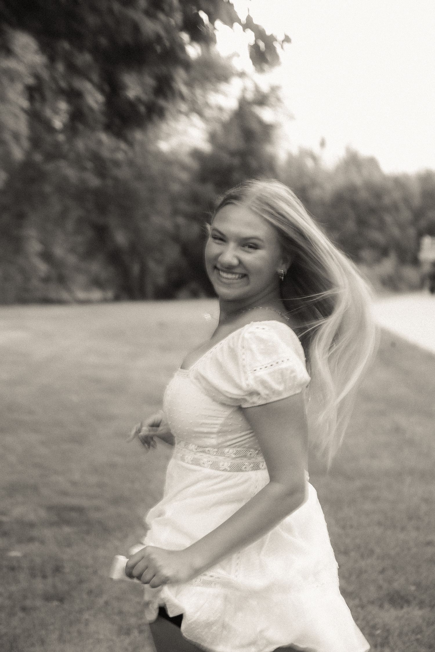 Whimsical black and white sequence of spinning and twirling in a flowing white dress on grassy field.