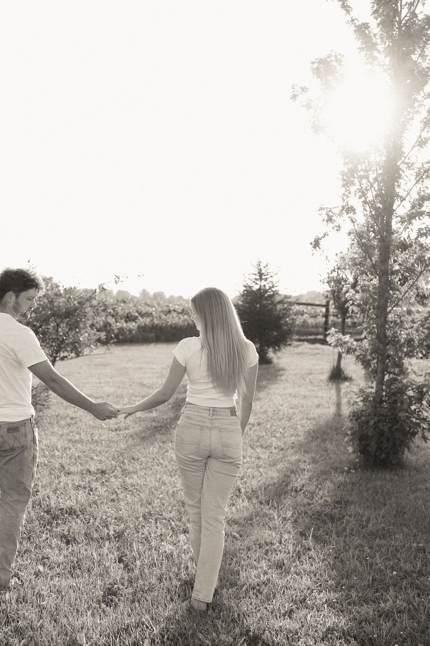 Couple walking hand in hand through a sunlit meadow in vintage-style photography.