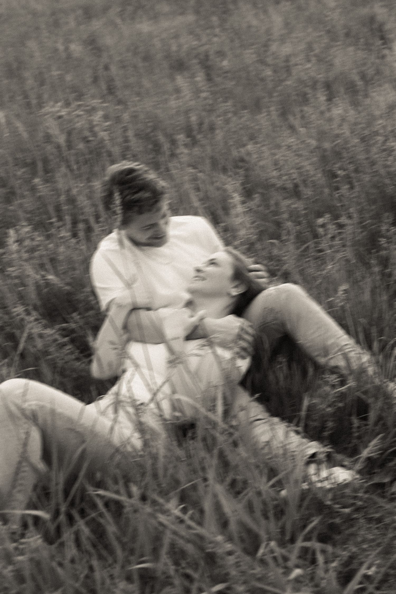 A romantic black and white photo of a couple laying in tall grass together.