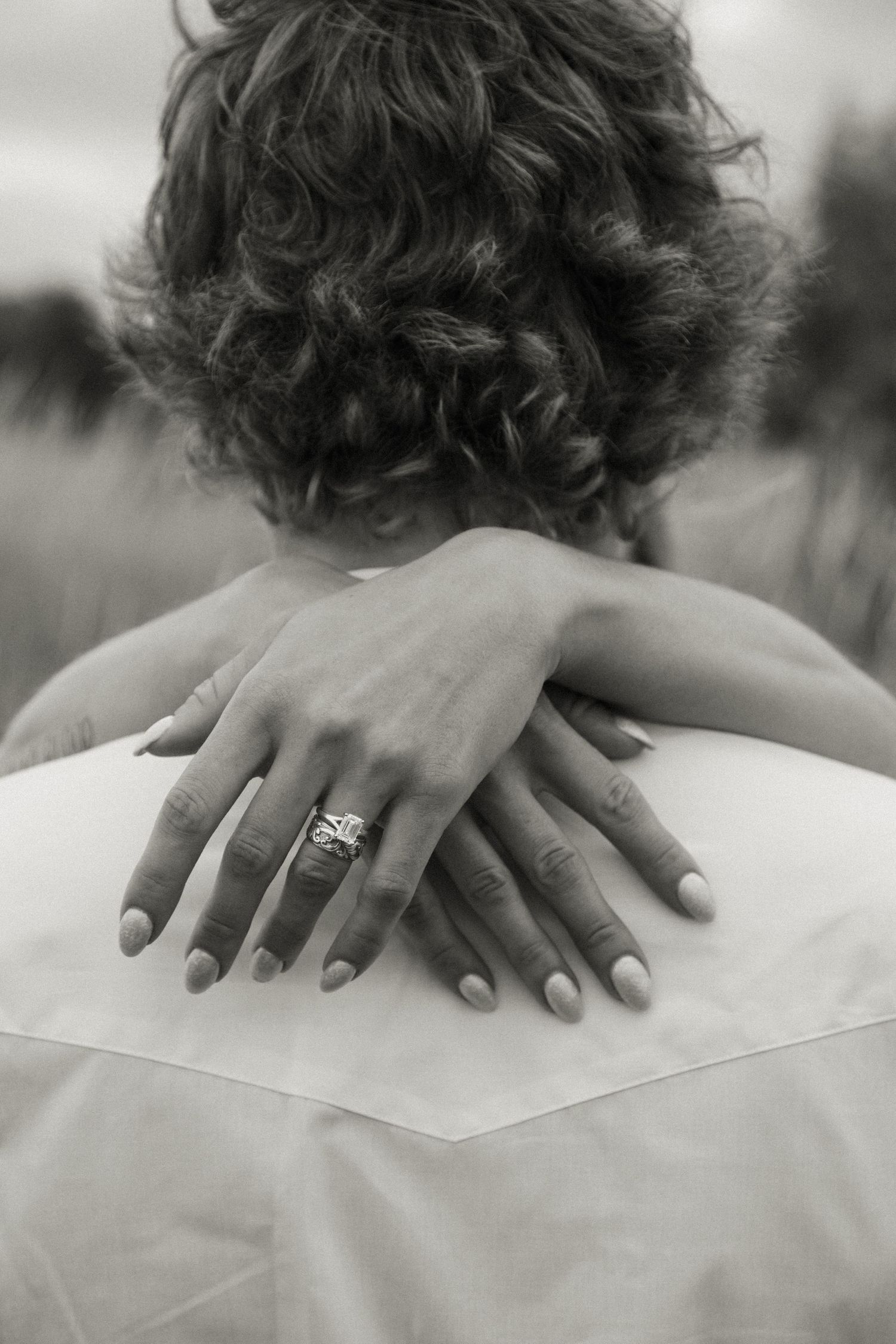 Close-up black and white photo of bride's hands with engagement ring embracing groom.