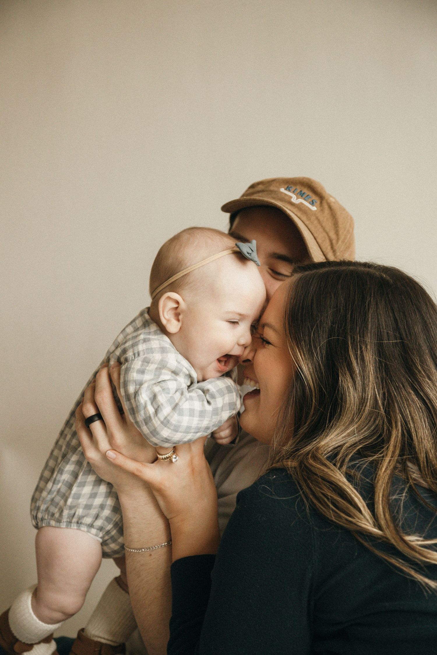 Happy parents kissing and cuddling their laughing baby girl in a warm, candid family portrait.