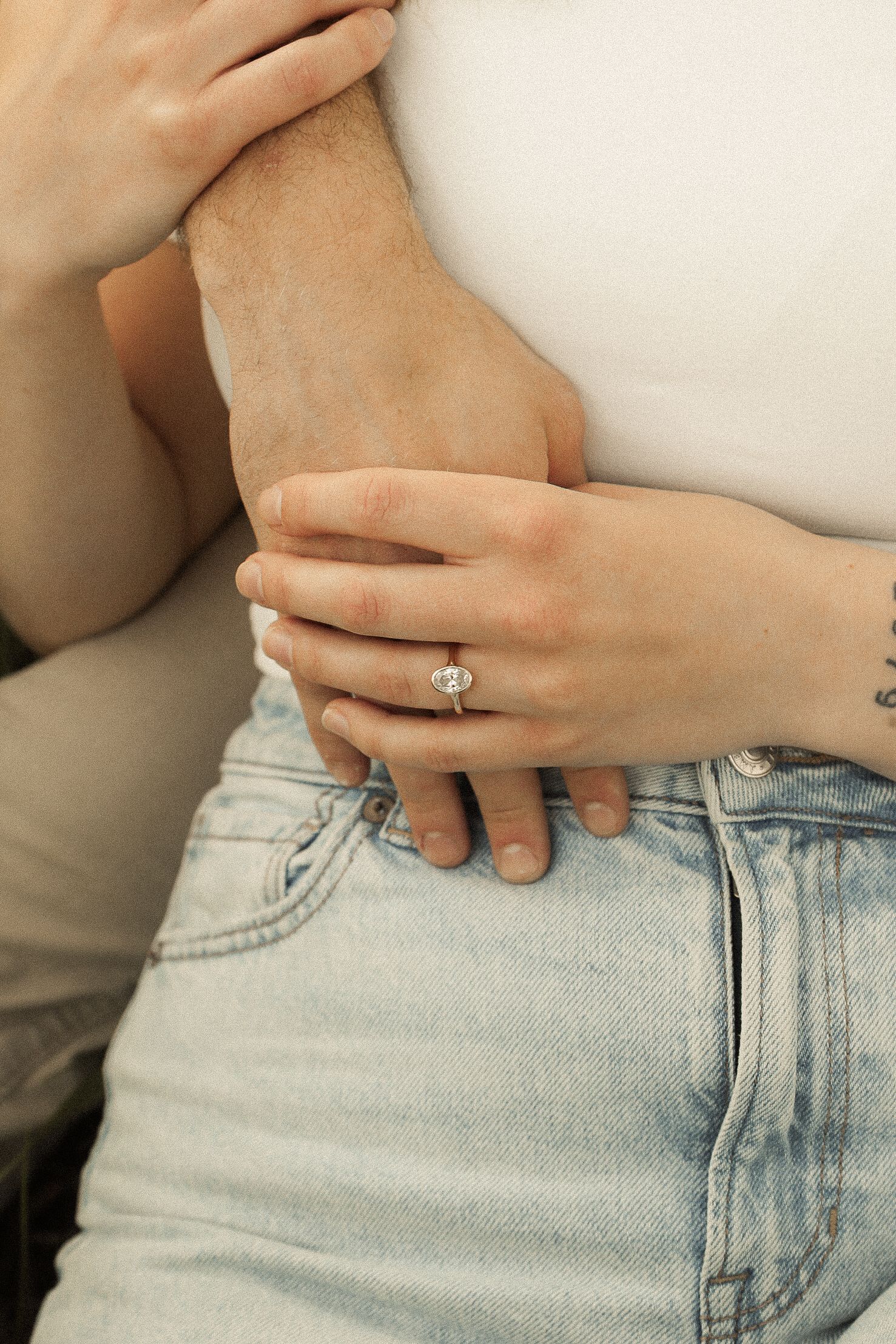 Close-up of hands resting on light wash denim jeans with an engagement ring visible.