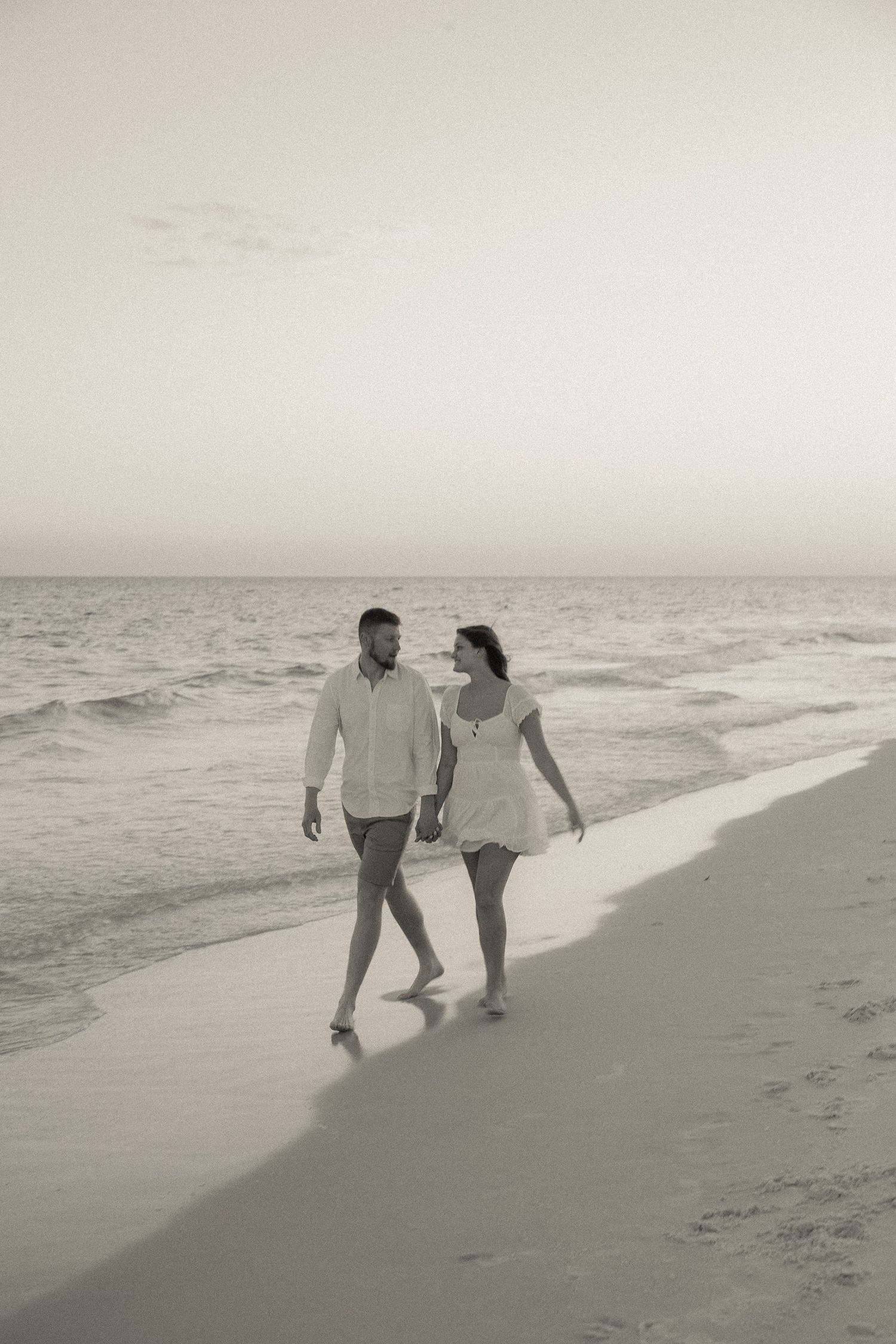 Couple walking together along a serene beach shoreline in black and white.