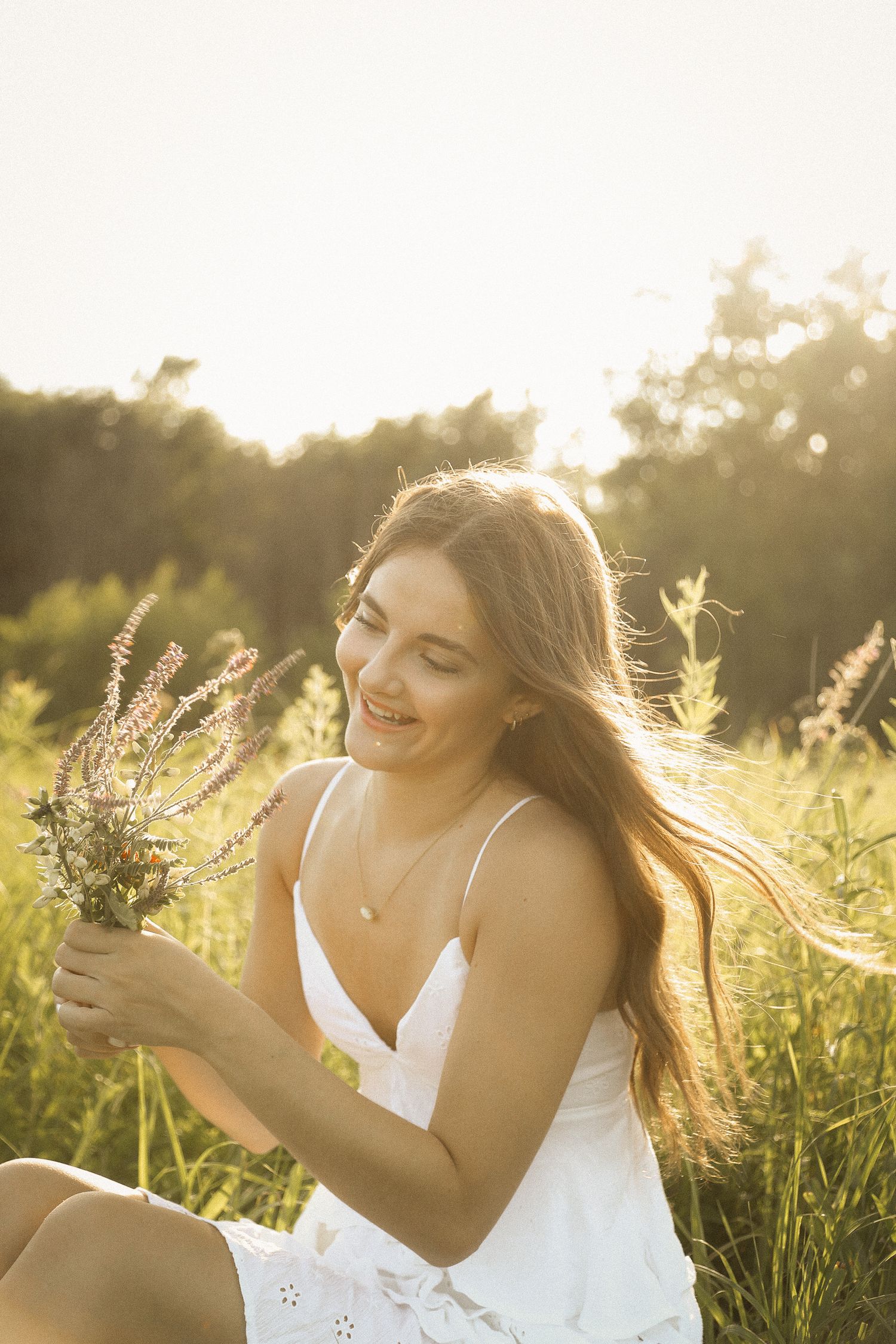 A white dress stands out against lush greenery during a golden hour photoshoot with wildflowers.