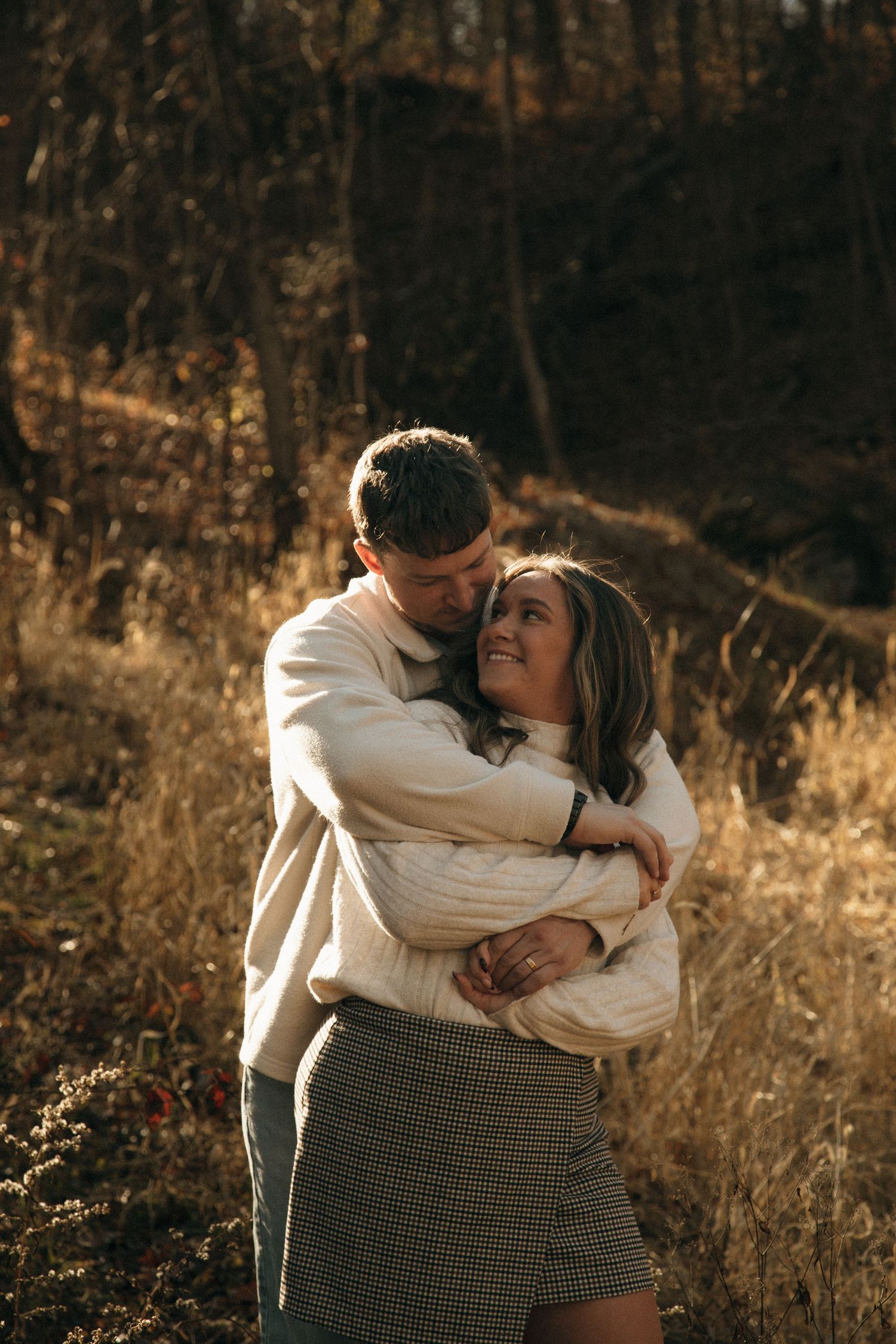 An intimate moment captured between a couple in casual attire against a warm autumn forest backdrop.