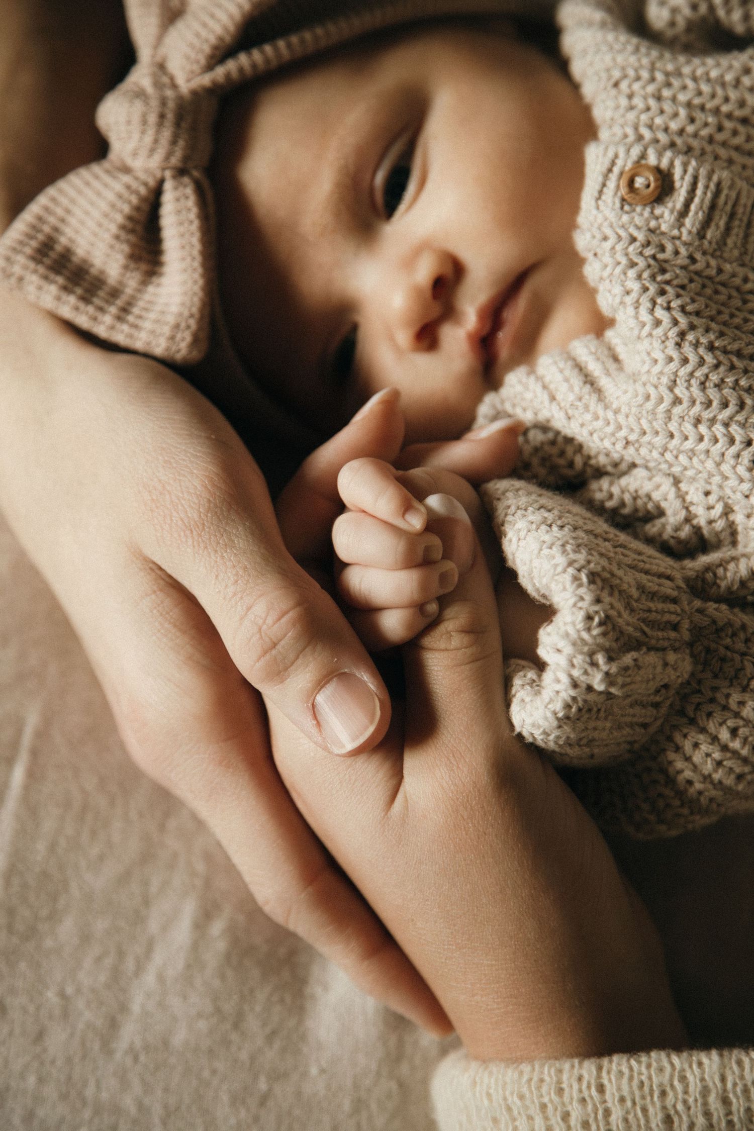 Gentle close-up of tiny newborn hands and knitted clothing details in soft natural light.