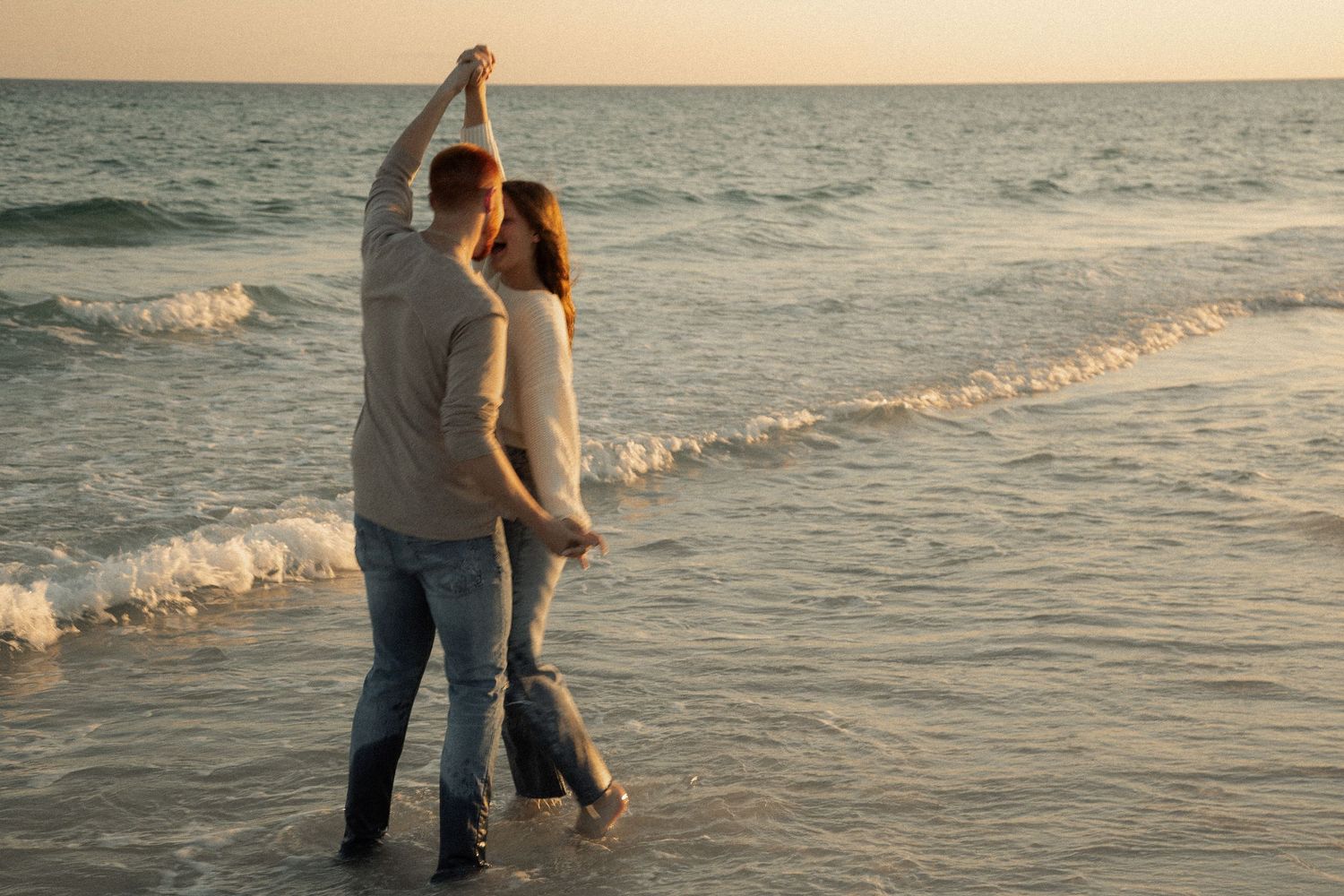 Two people wading into gentle ocean waves during golden hour.