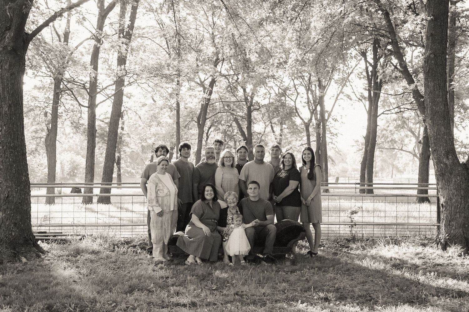 A large group sits together under trees for an outdoor gathering.