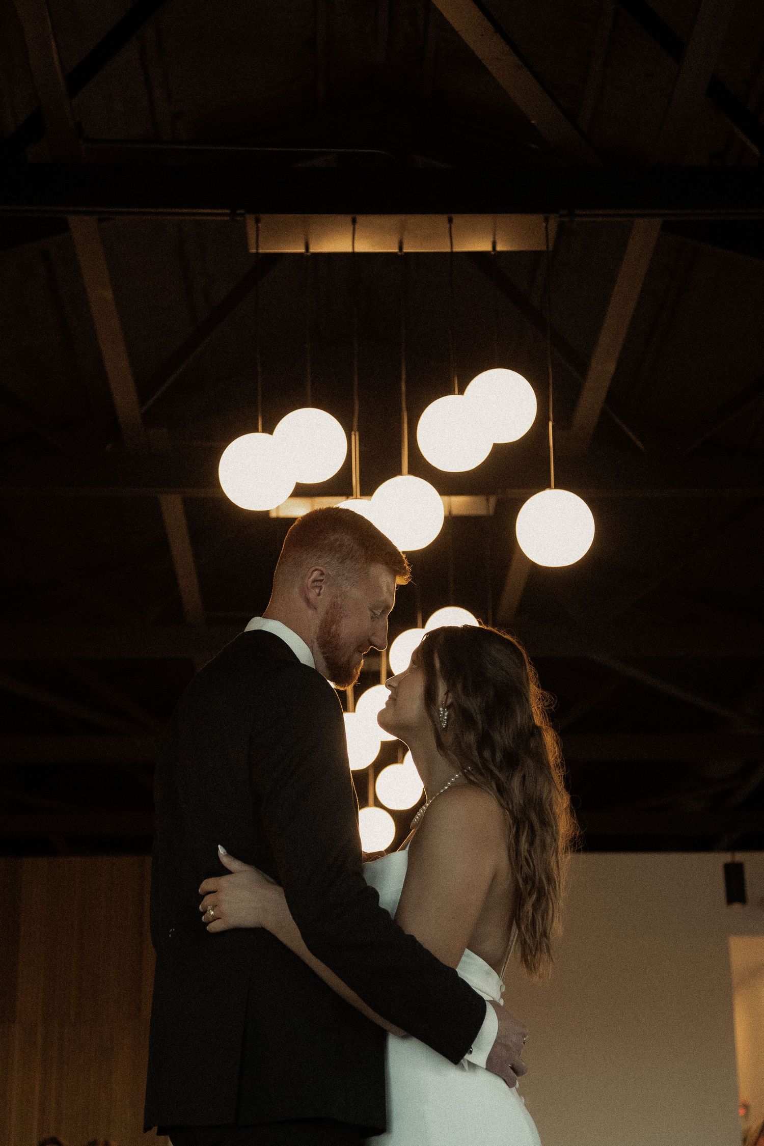 Couple dancing under glowing round pendant lights in a romantic setting.