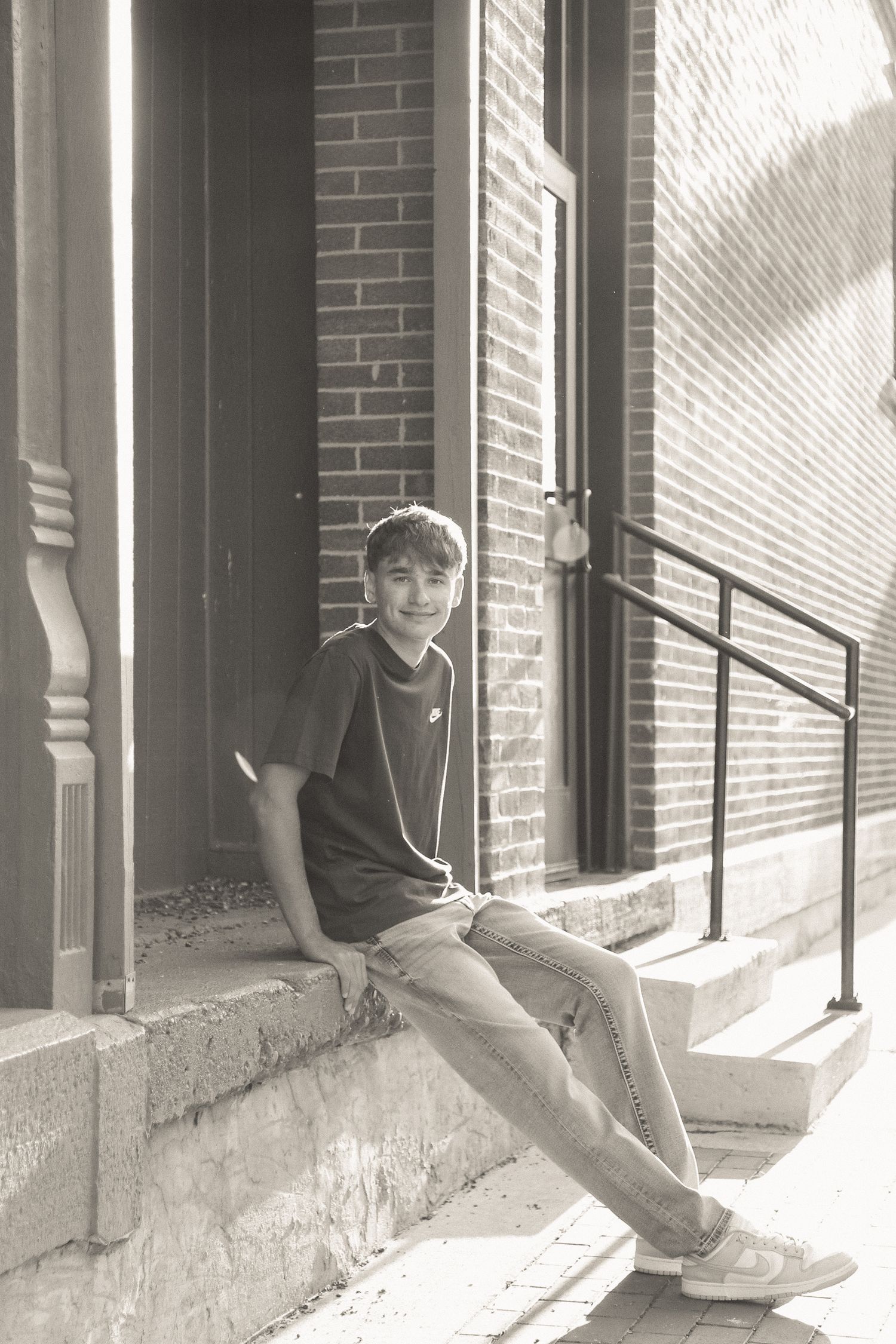 Black and white photo of person sitting on brick building ledge with dramatic shadows.