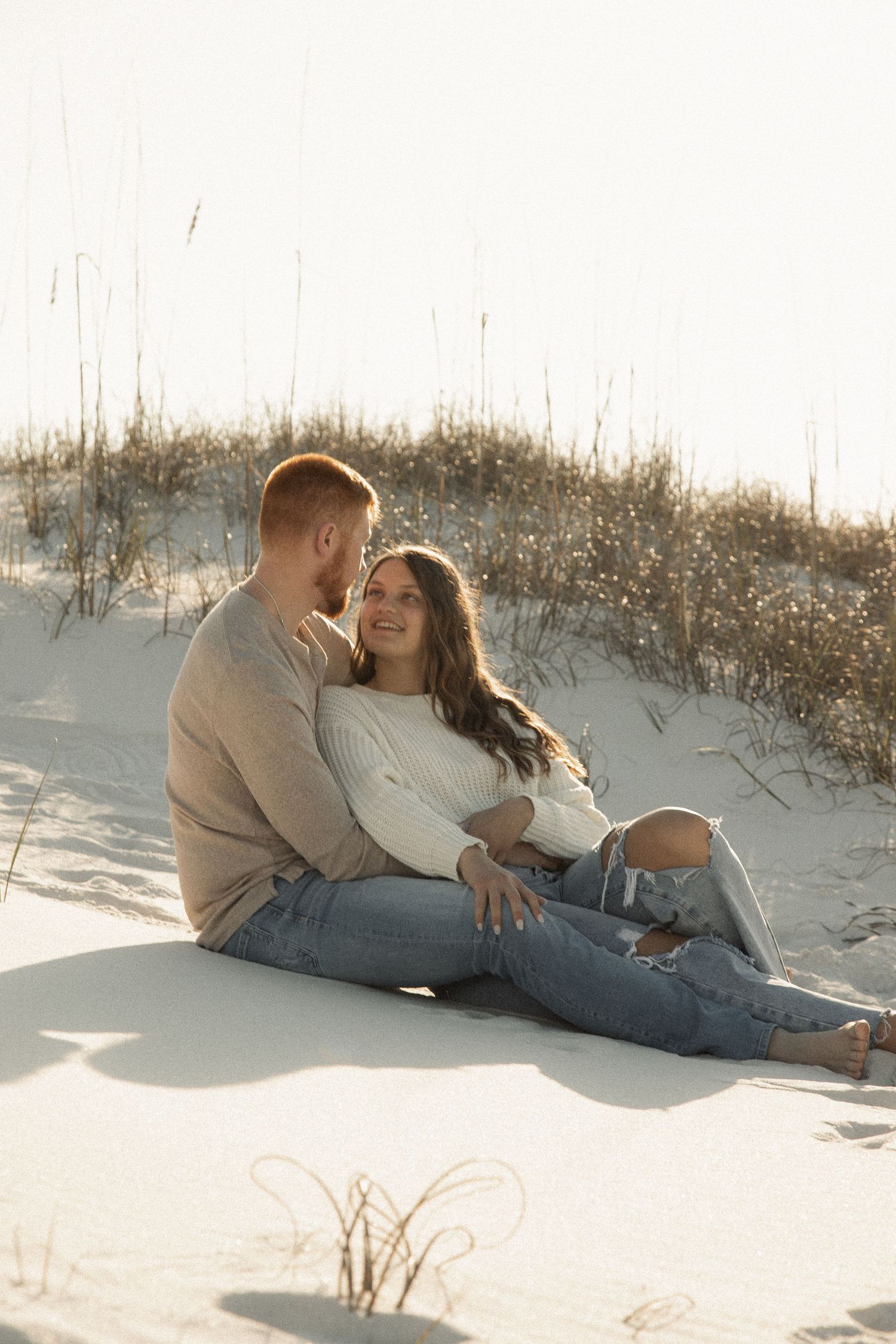 Couple relaxing together on white sand dunes in casual winter attire.