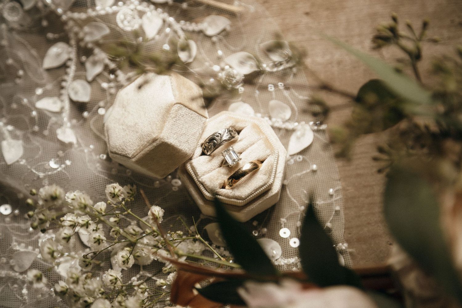 Elegant wedding rings displayed in a vintage velvet ring box surrounded by delicate white flowers and greenery.