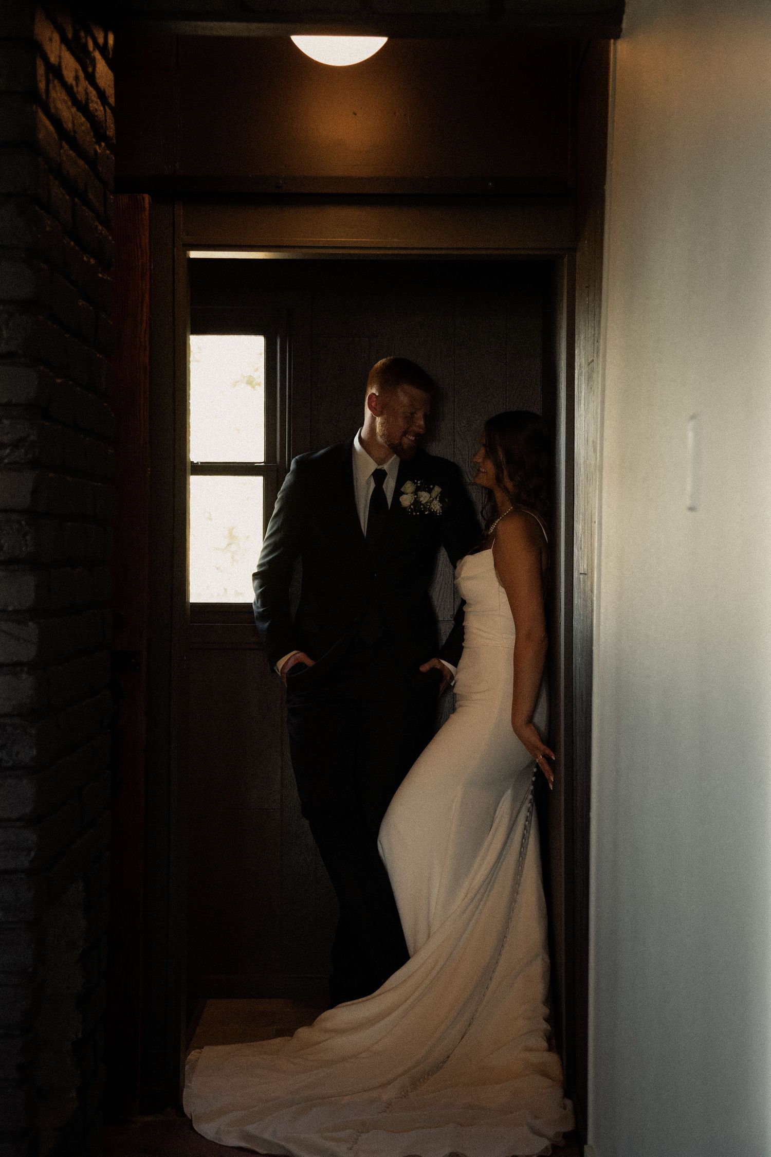 Wedding couple in silhouette standing in a brightly lit doorway.