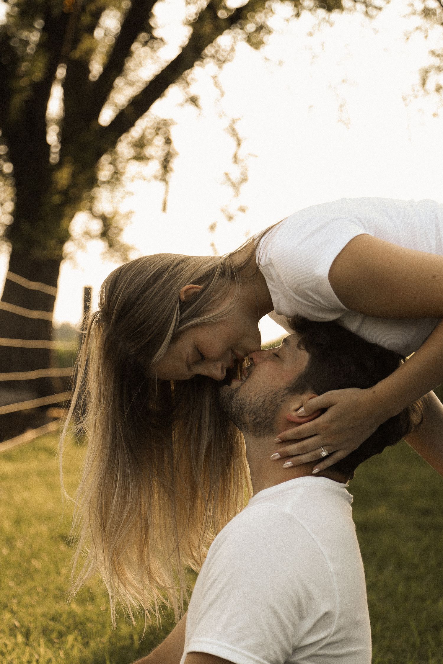 A romantic couple shares an intimate kiss in a sun-drenched outdoor setting.