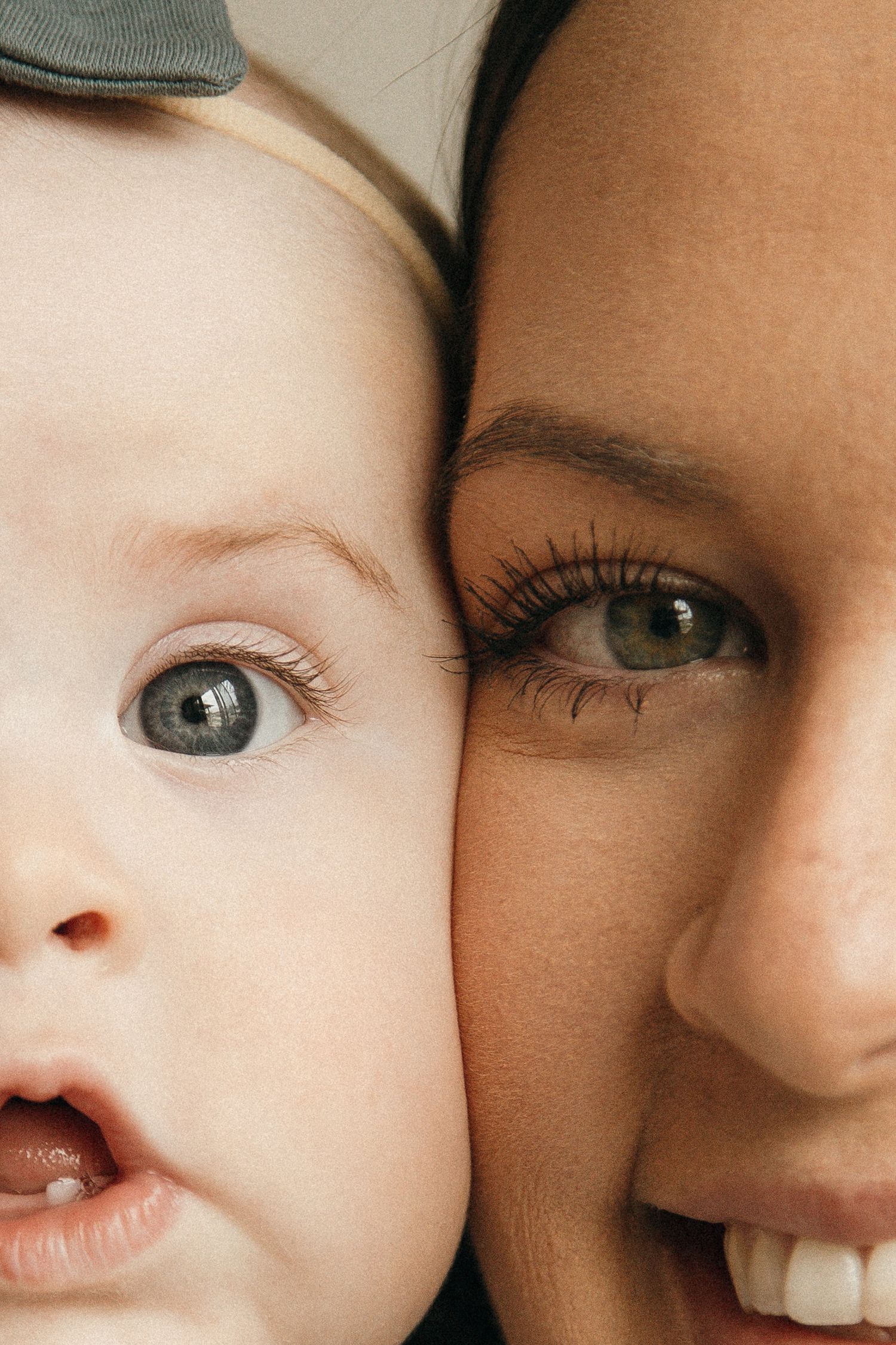 Close-up portrait of a smiling mother cheek-to-cheek with her blue-eyed baby, both looking forward.