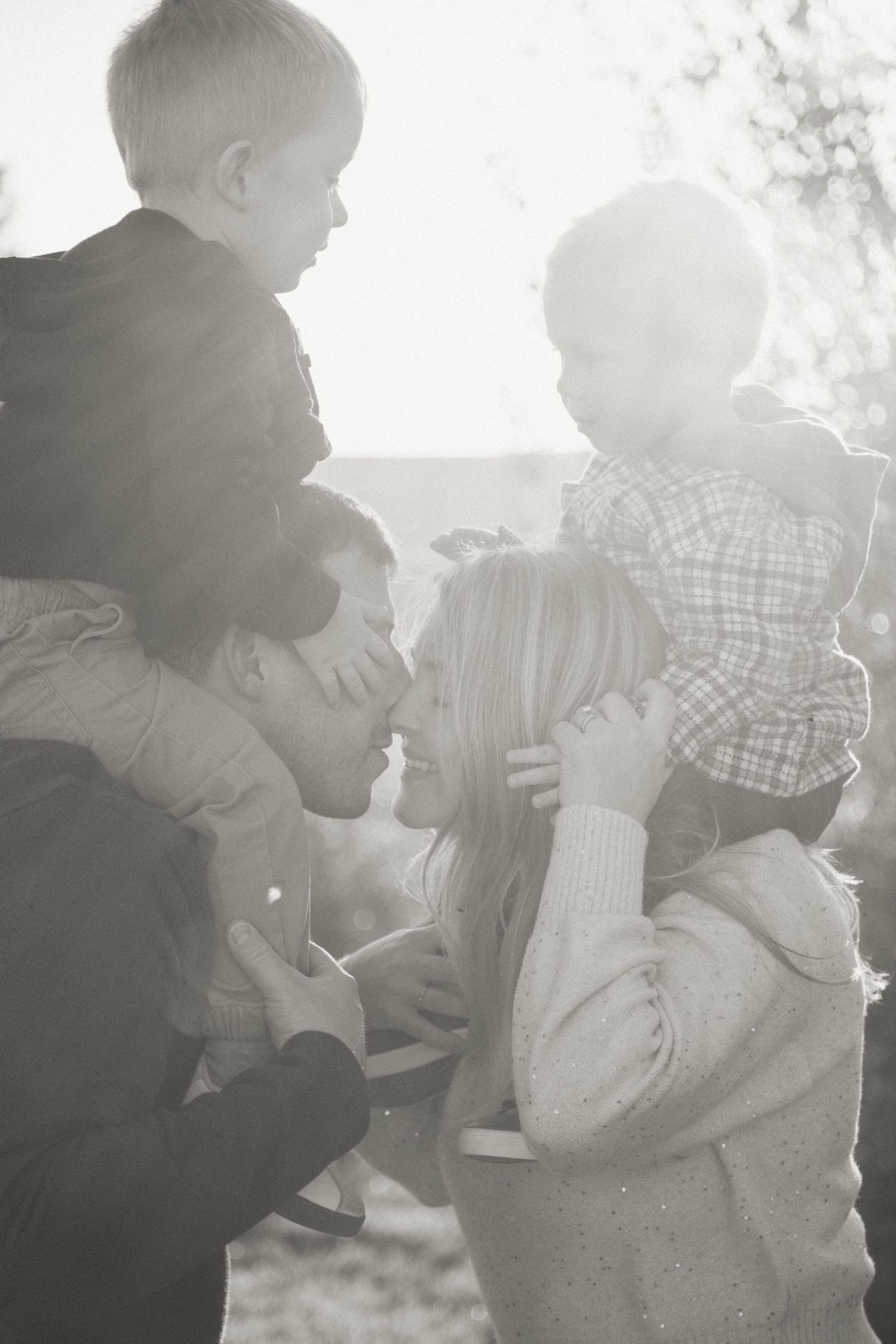 Black and white portrait of a family sharing an intimate moment outdoors in natural light.