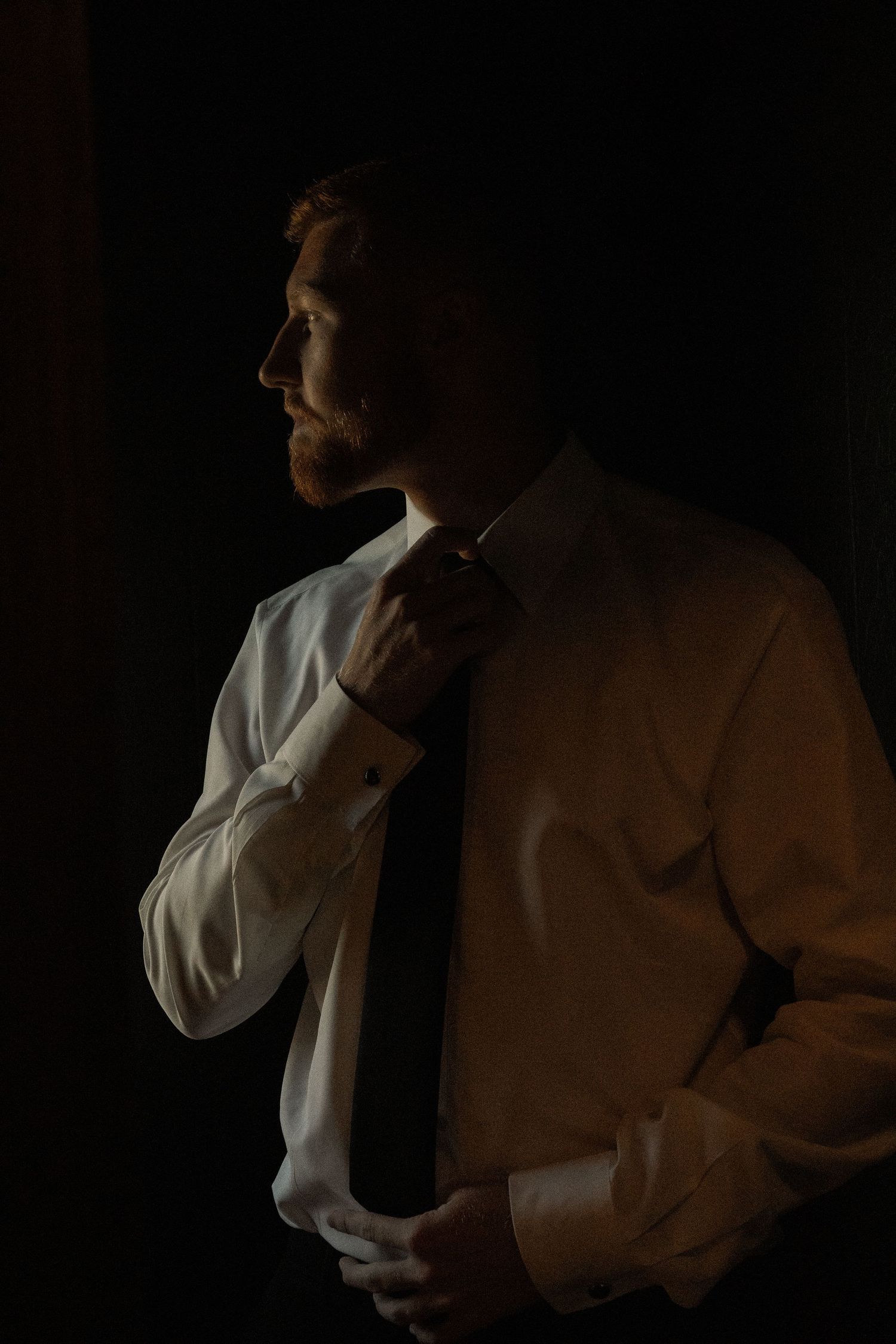 Moody silhouette portrait in low light against a dark background.
