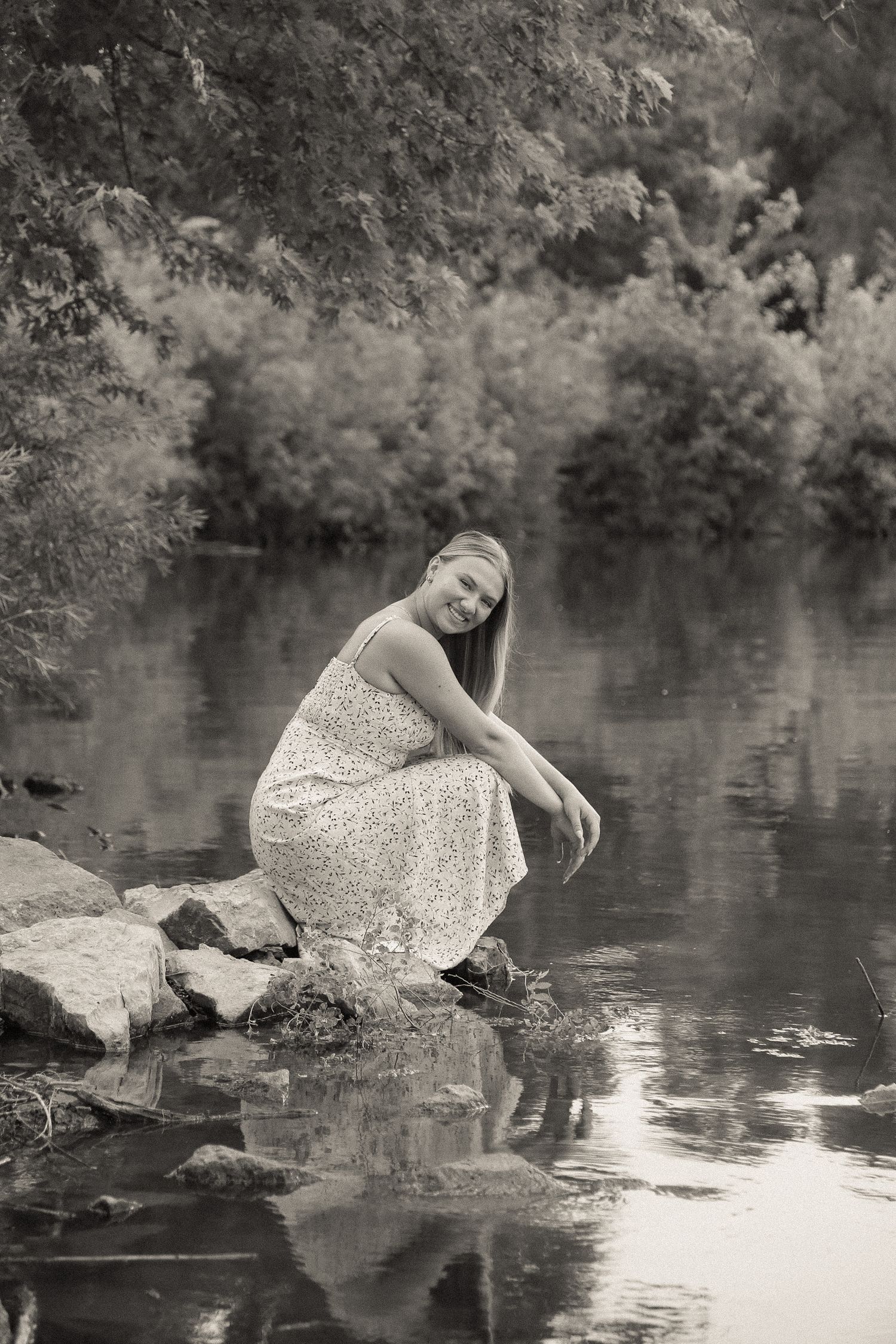 Dreamy black and white scene of someone in floral dress playing by water's edge.