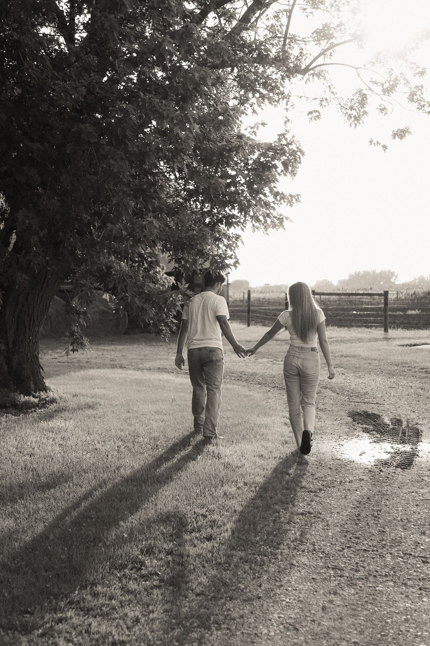 Black and white photo of two people walking hand in hand along a country path at sunset.