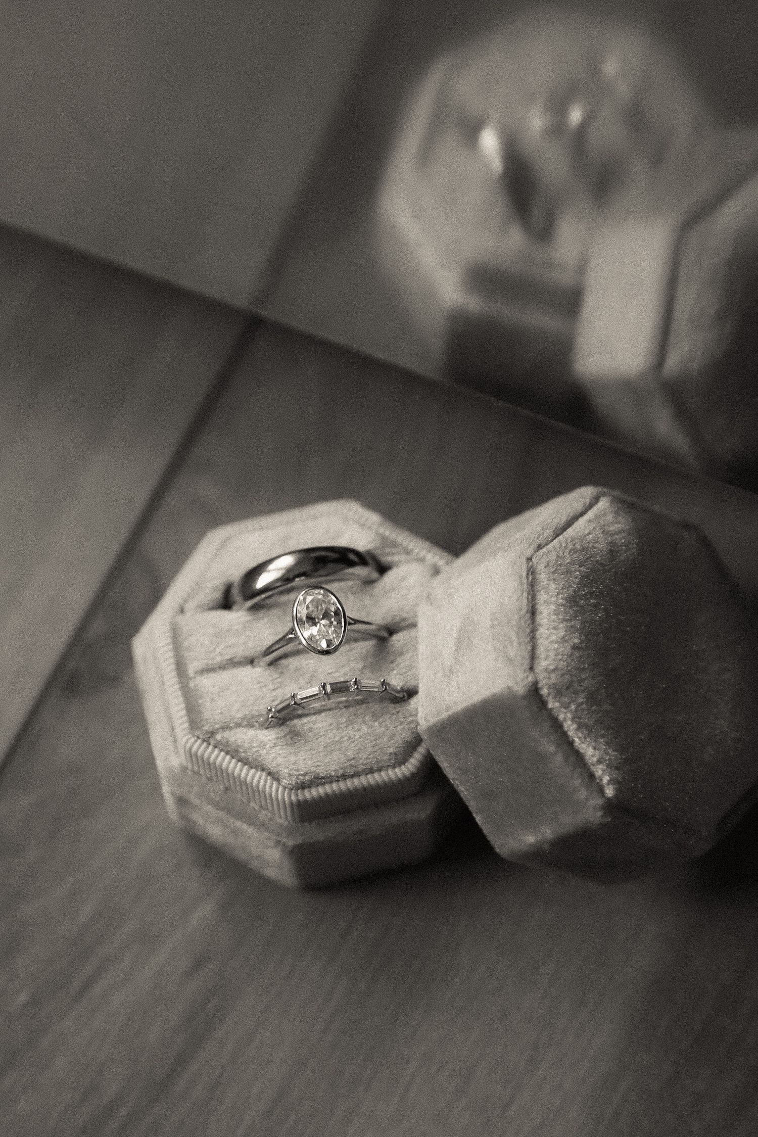 A vintage engagement ring sits in a gray velvet hexagonal ring box on a wooden surface.
