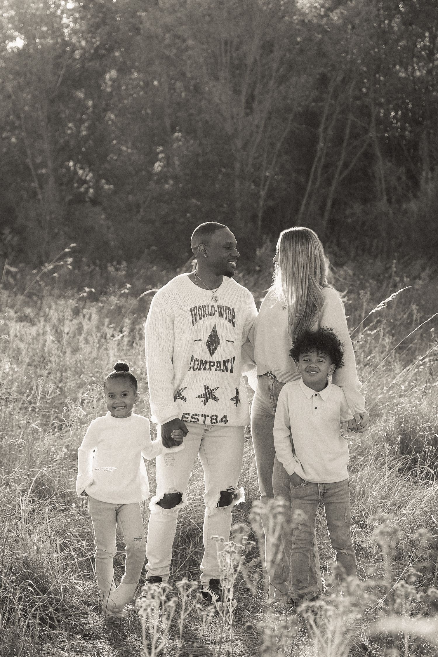 A family of four poses together in a field of tall grass during an outdoor photo session.