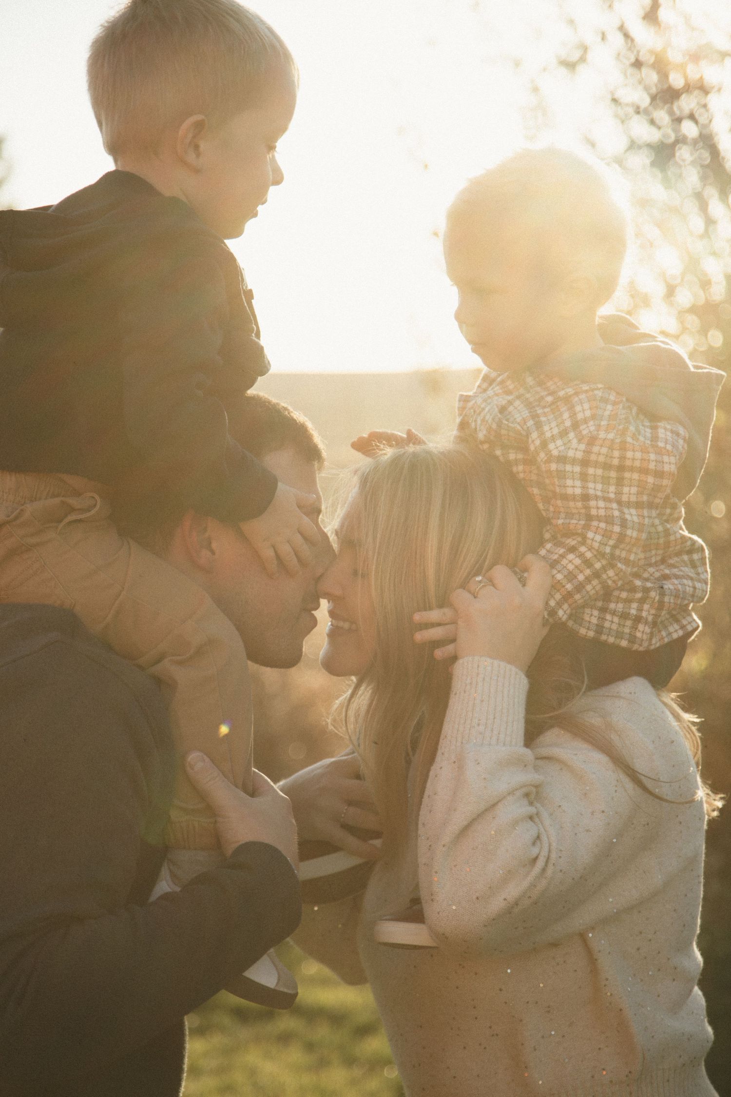 Family sharing joyful moments together in backlit golden sunlight outdoors.