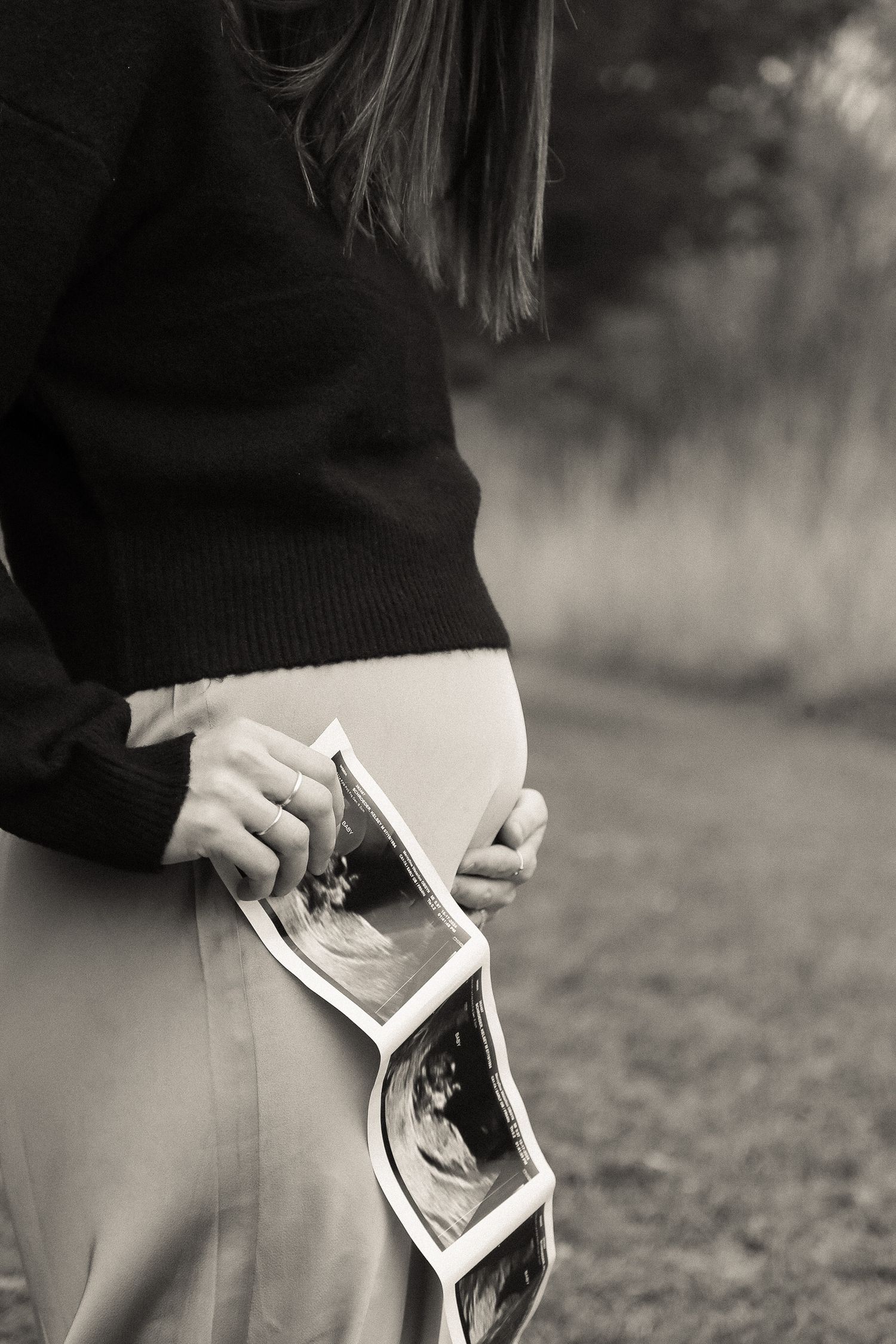 A side view of someone holding ultrasound images against their belly in black and white.
