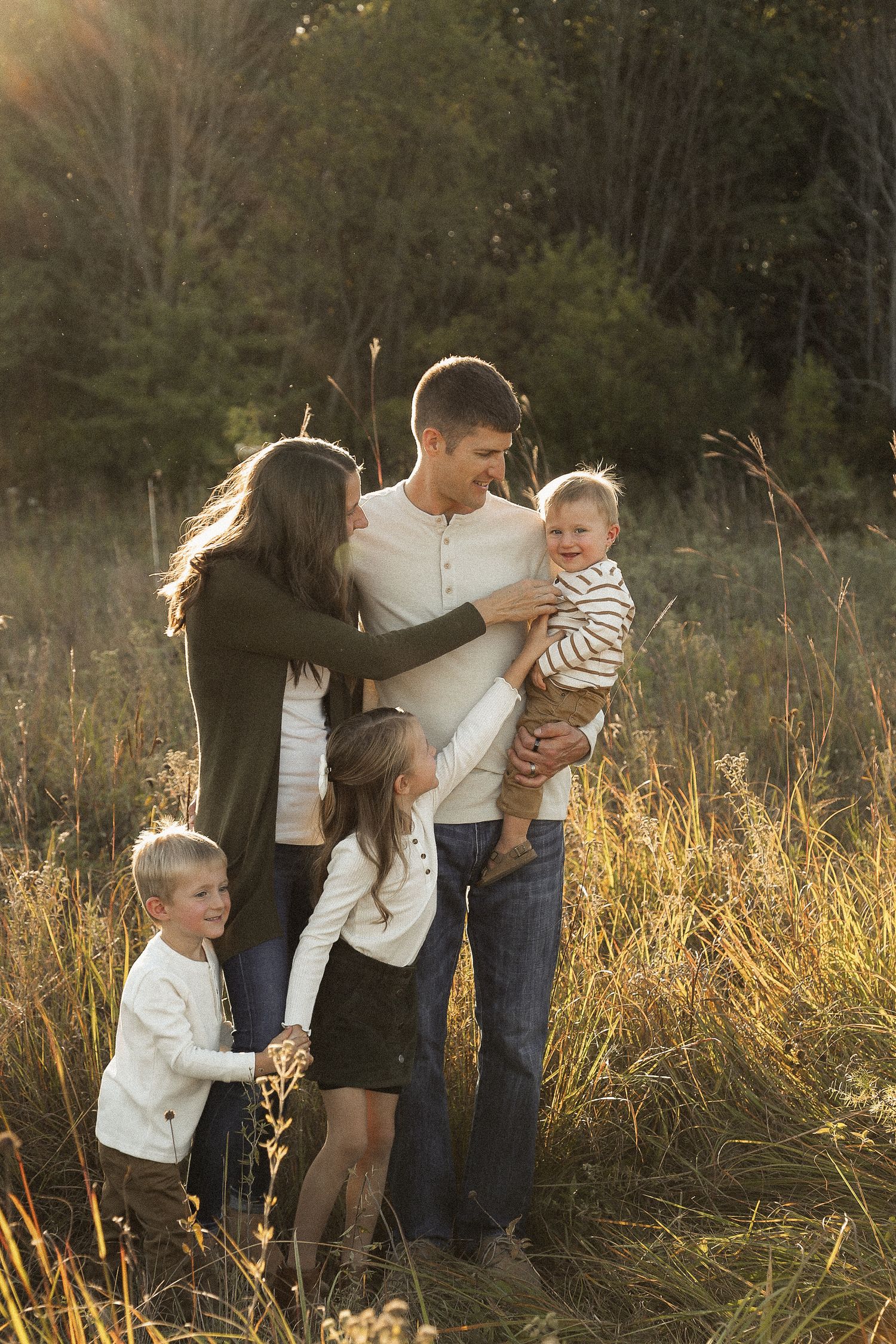 Family playing and interacting in a golden field during sunset.