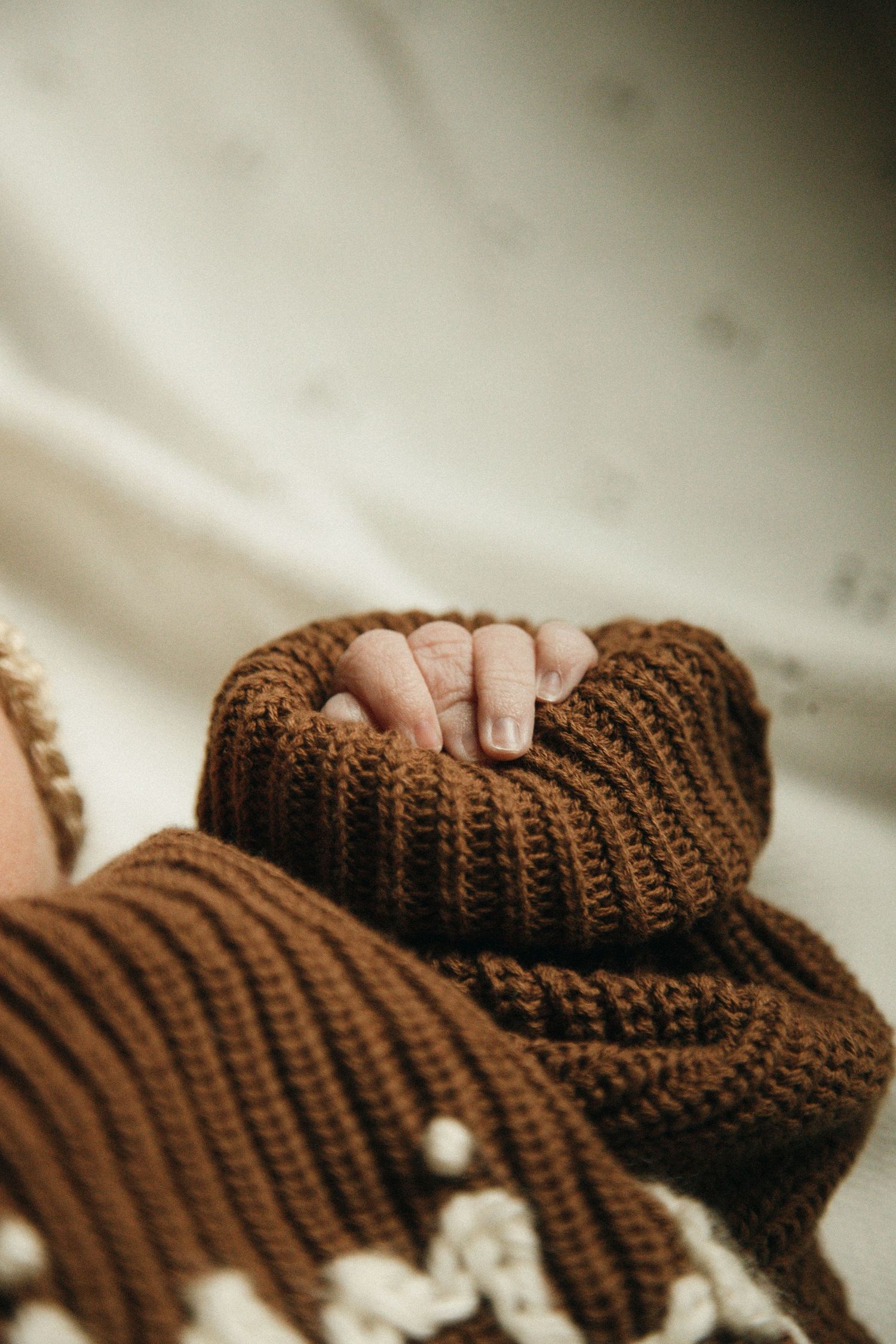 Close-up detail of tiny fingers grasping a brown knitted blanket texture.