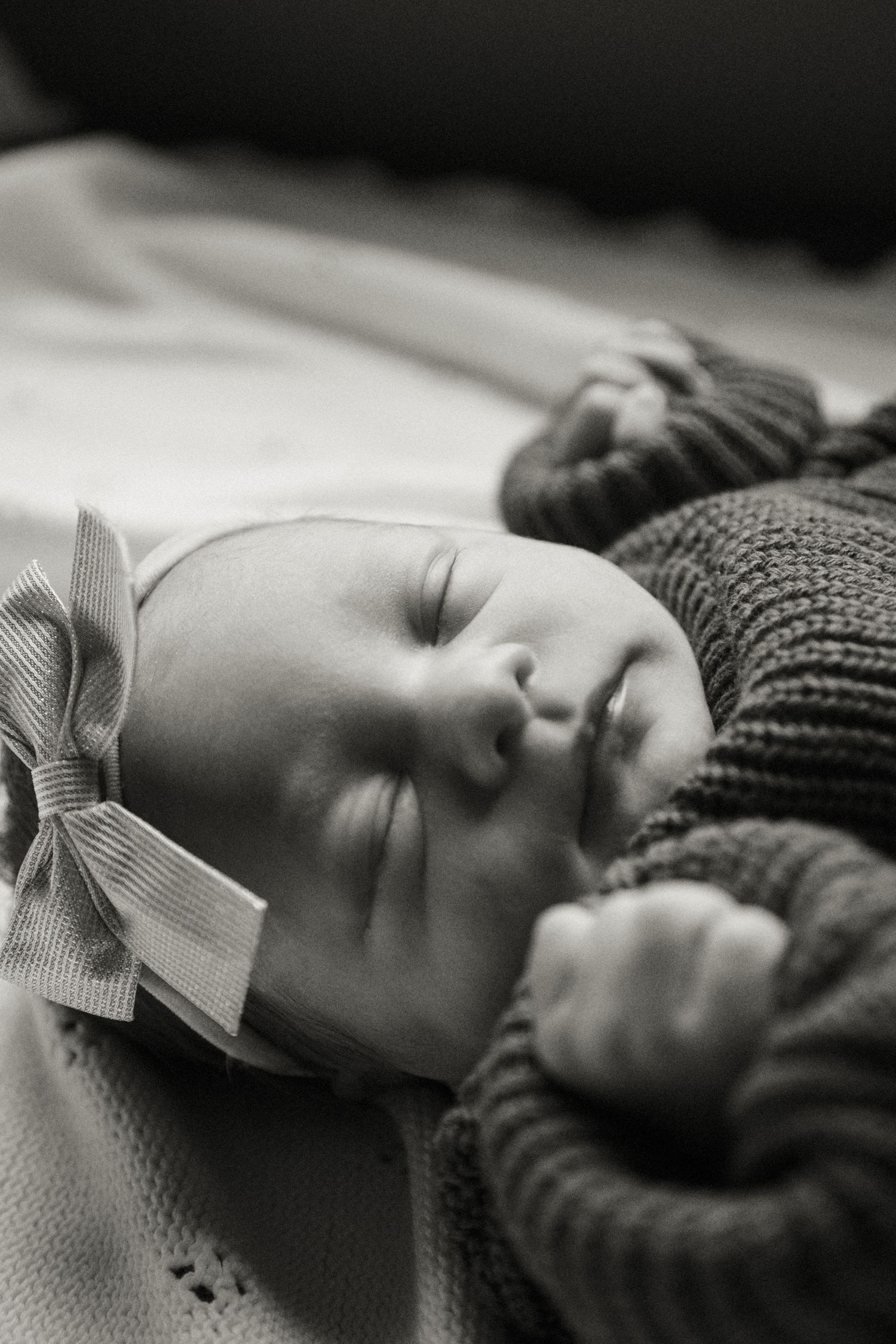 Peaceful black and white portrait of a sleeping baby wearing a knit hat with bow detail.