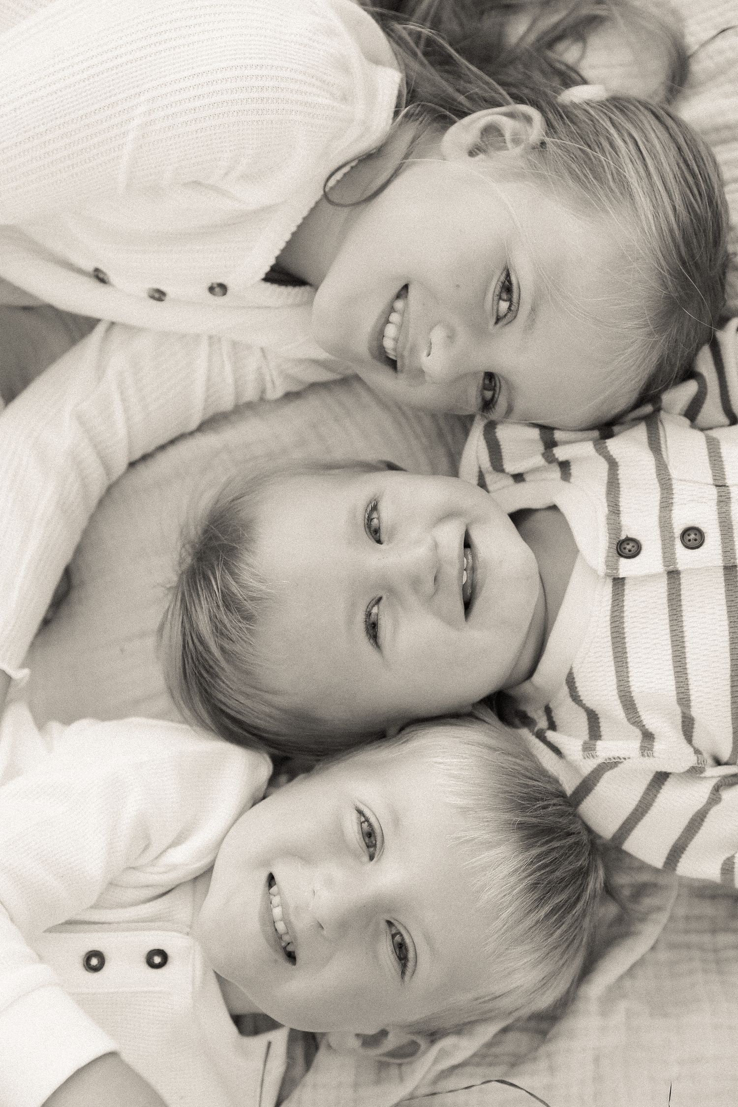 Black and white portrait of children lying down on soft fabric.